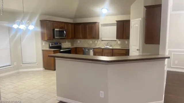 Kitchen featuring wood-finish cabinetry, stainless steel appliances, tile backsplash, and a breakfast bar