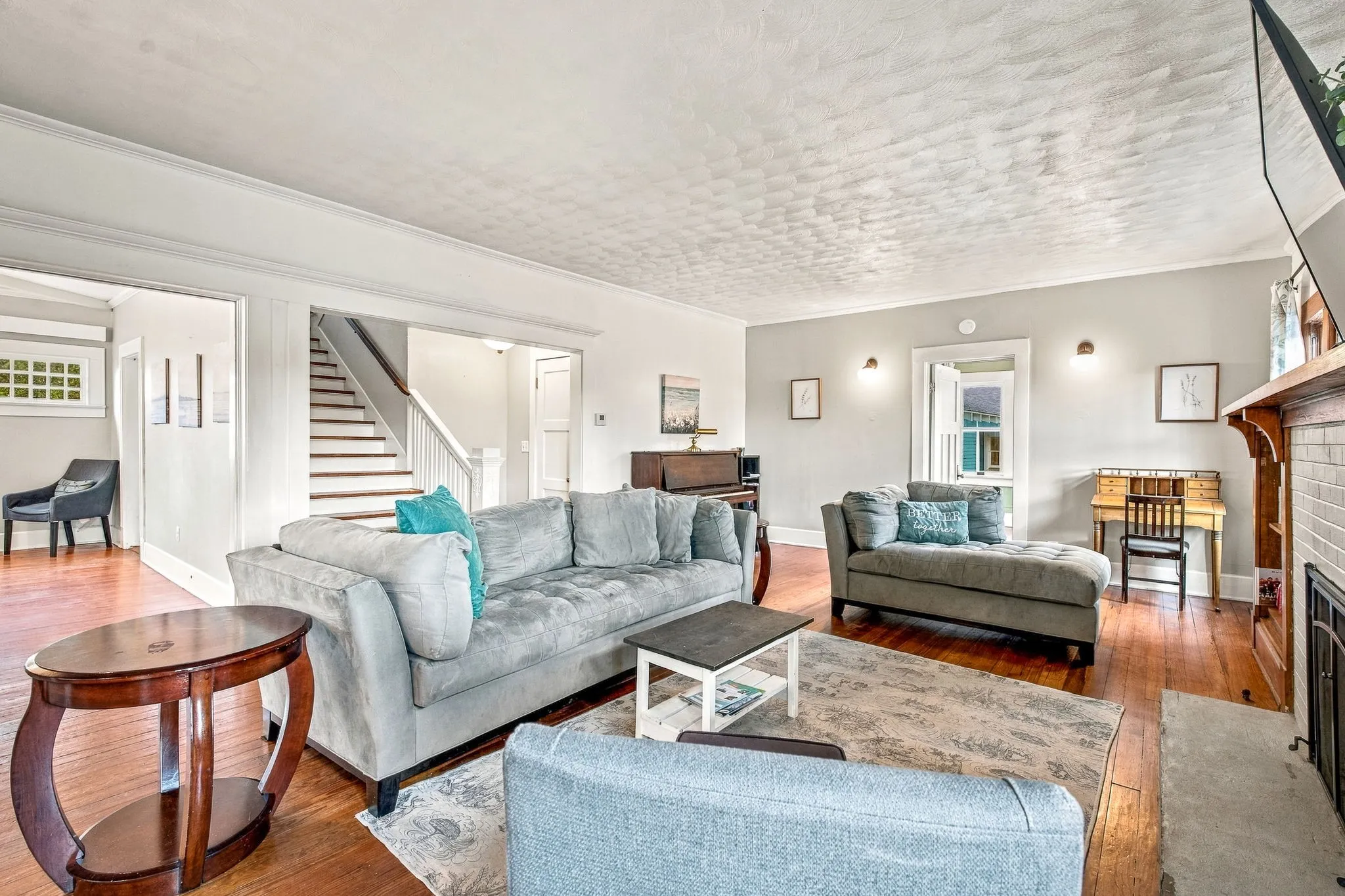 Hardwood flooring, painted white walls, recessed wall sconces, fireplace with a tile surround and wood mantel, and a multi-level staircase with white risers and wood treads