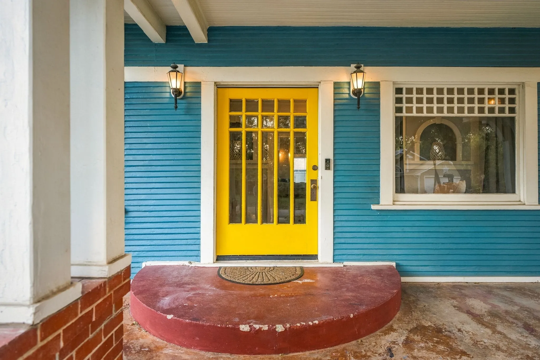 Vibrant yellow paneled entry door with sidelights, blue horizontal siding, and a decorative transom window