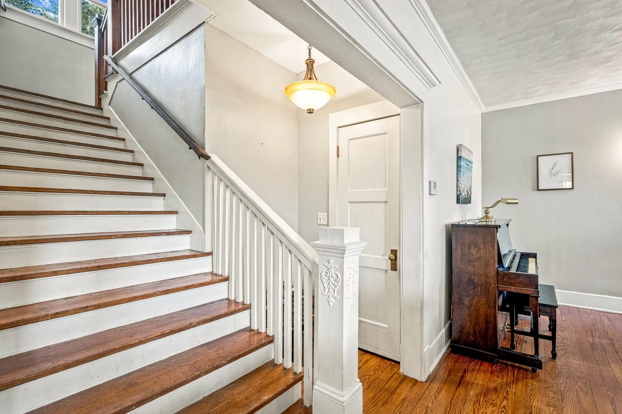 Hardwood flooring, painted white staircase, wood handrail, traditional spindle balusters, and a decorative newel post