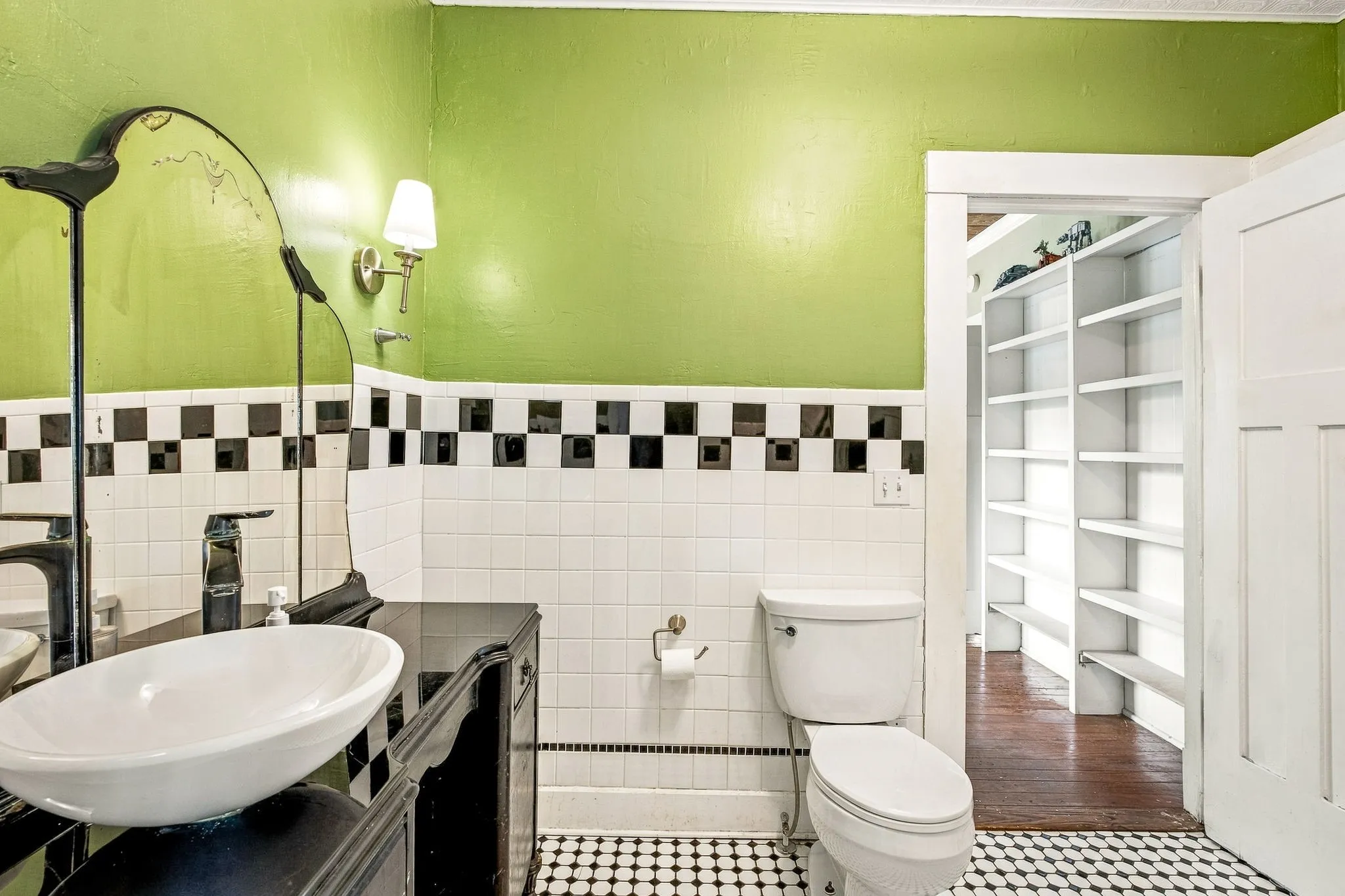 Bathroom featuring a vessel sink, black vanity, wall-mounted sconce, and checkered tile flooring