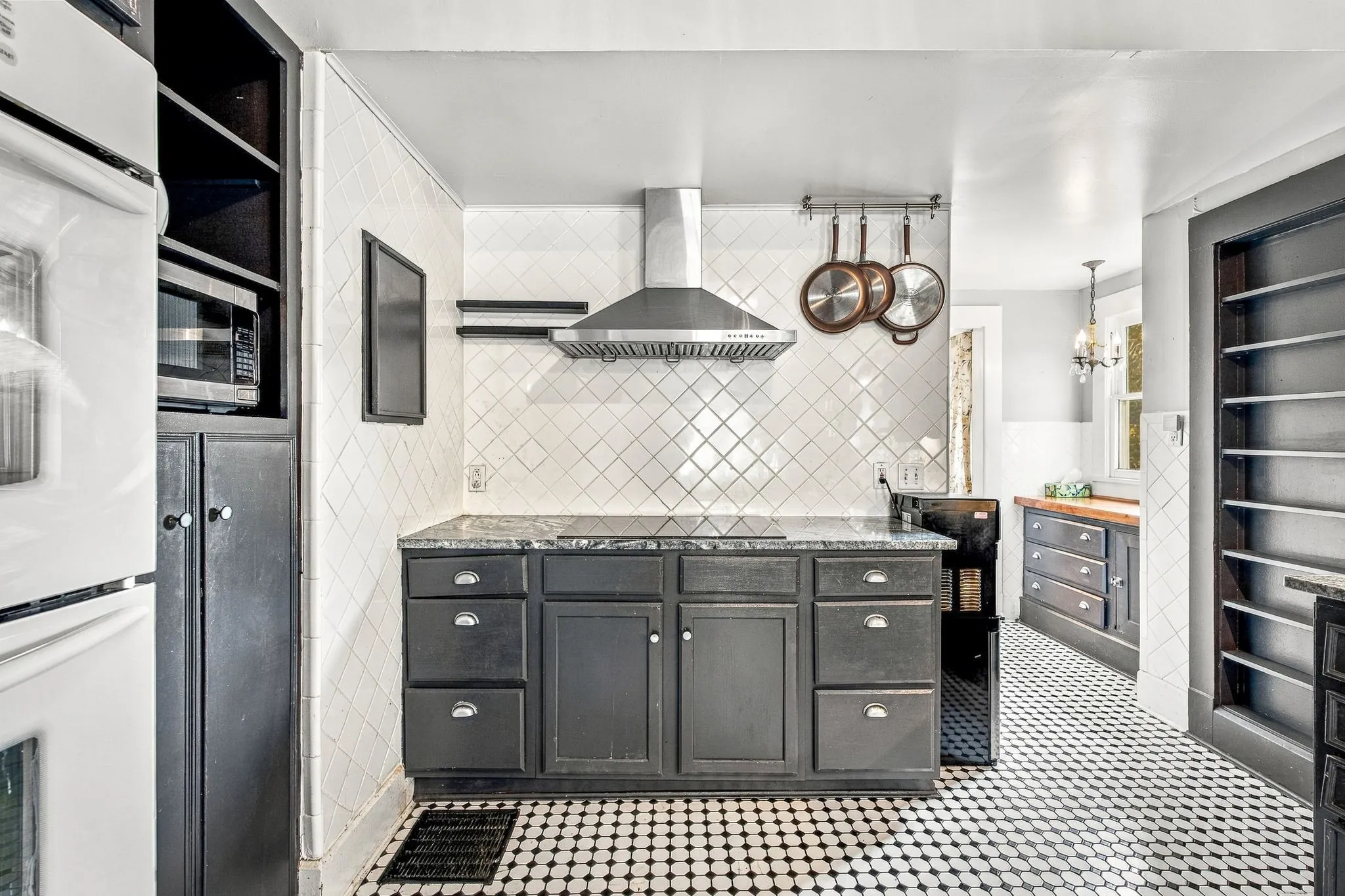 Kitchen featuring black cabinetry, patterned tile flooring, white subway tile backsplash, stainless steel range hood, and solid surface countertops