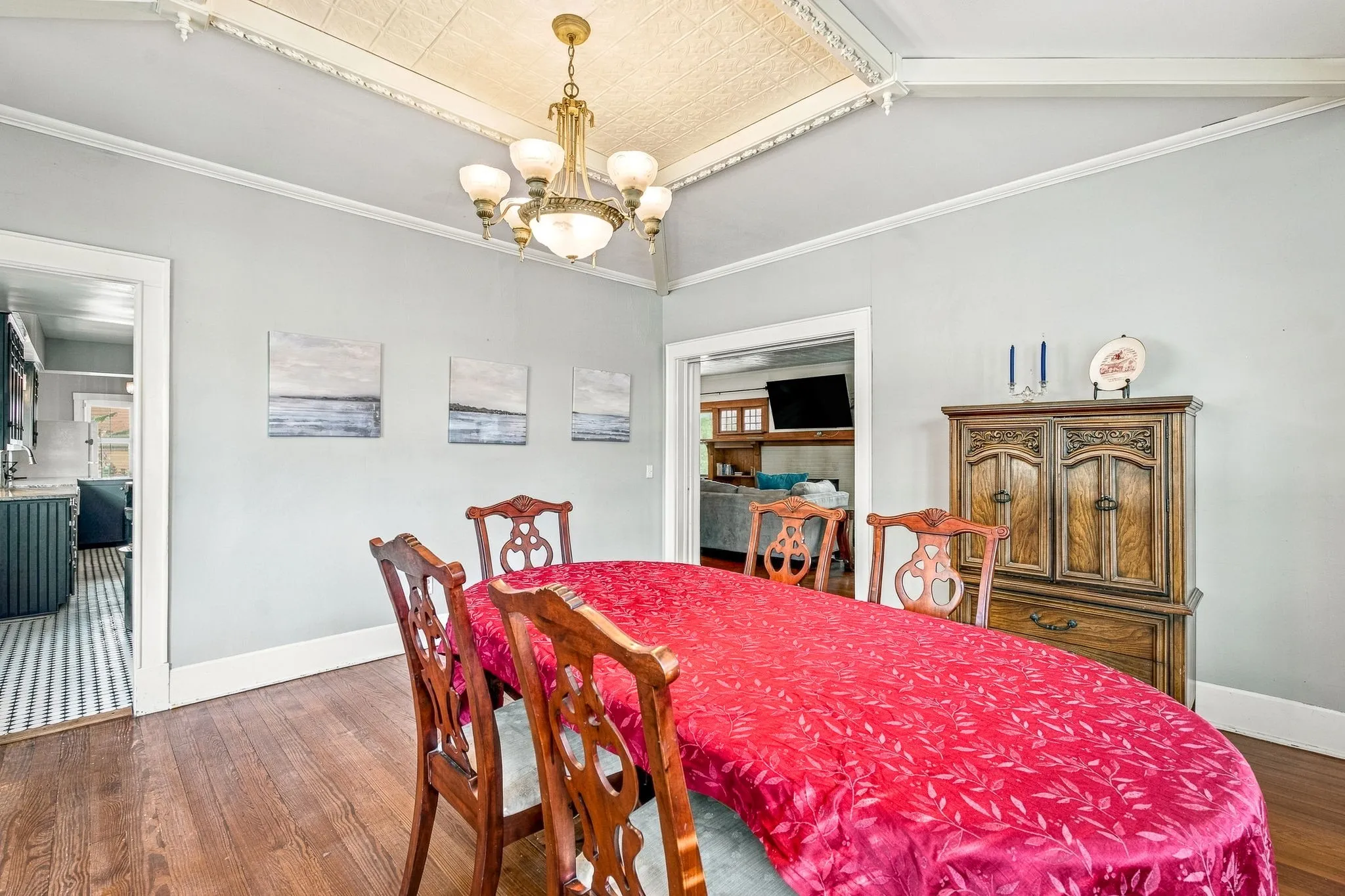 Formal dining room showcasing hardwood flooring, a brass chandelier with frosted glass shades, and soft gray wall finishes