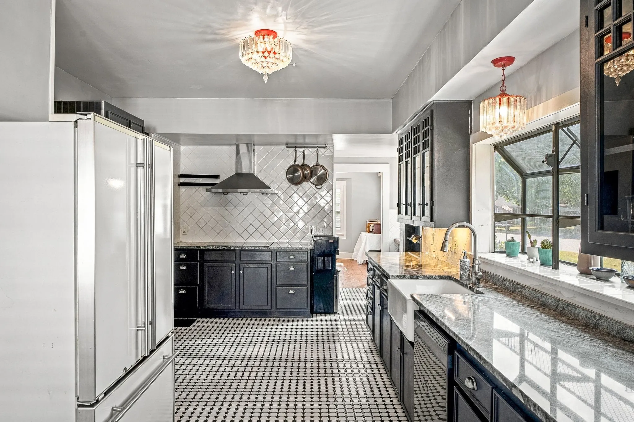 Galley kitchen featuring black cabinetry with brushed metal hardware, geometric tile backsplash, stainless steel range hood, dual pendant lighting, quartz countertops, and geometric patterned tile flooring
