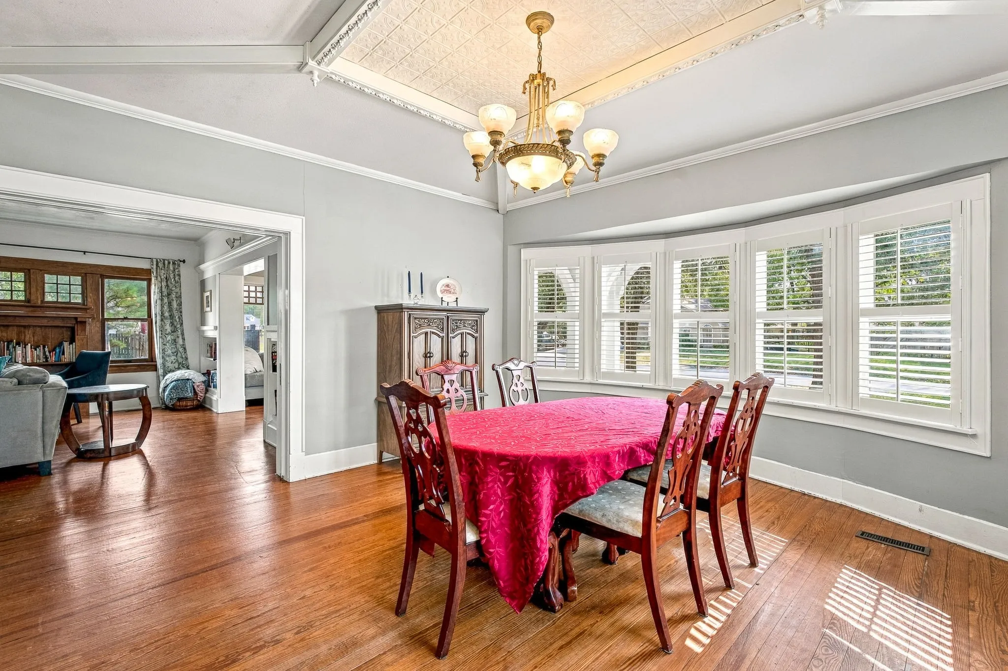 Hardwood flooring, bay window with multiple panes, crown molding, white trim, and a decorative ceiling fixture