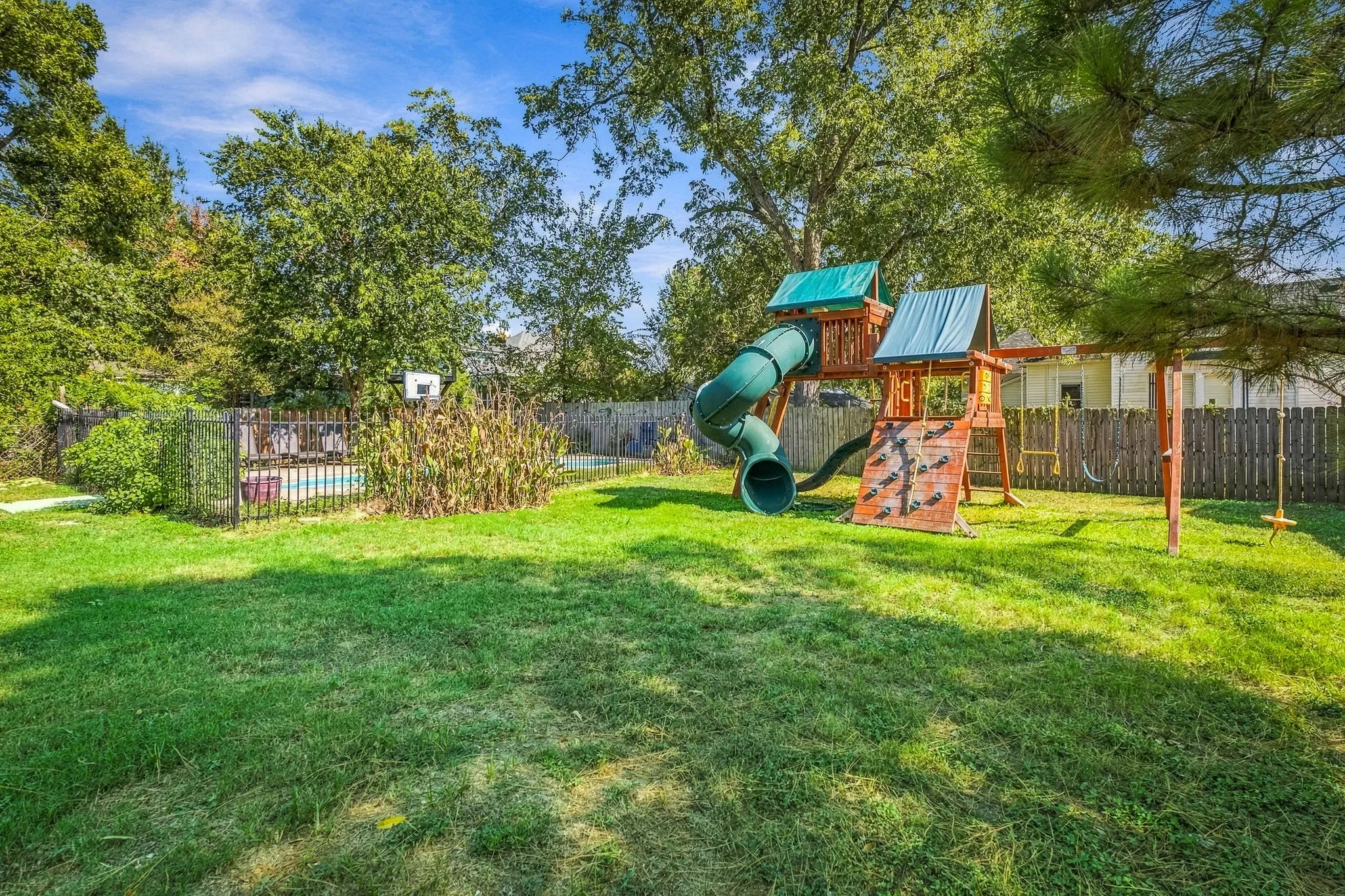 Expansive backyard featuring a manicured lawn, a secured pool area with fencing, and a wooden privacy fence
