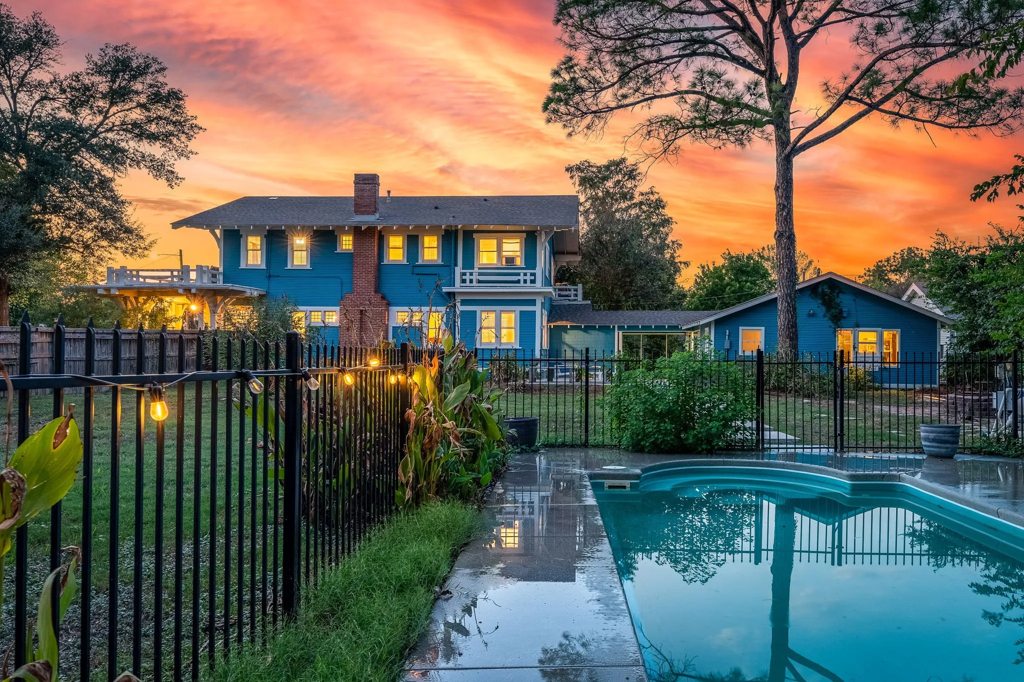 Expansive backyard featuring a swimming pool, black metal fencing, and mature trees