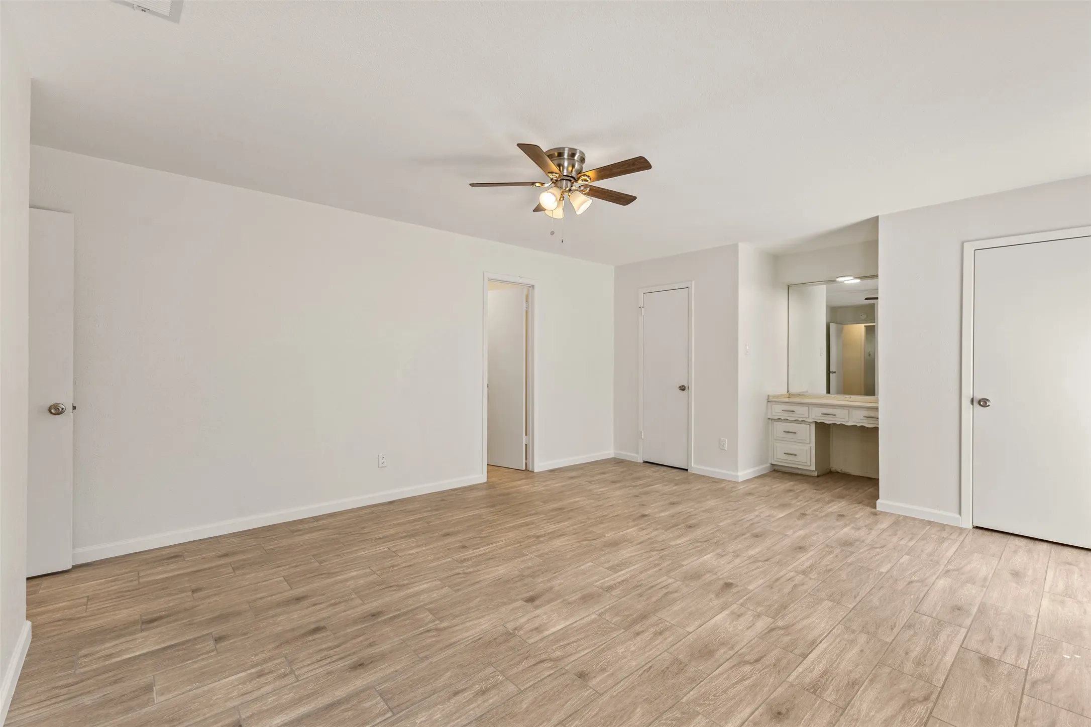 Spacious room with wood-finish flooring, a ceiling fan, and a built-in vanity with mirror