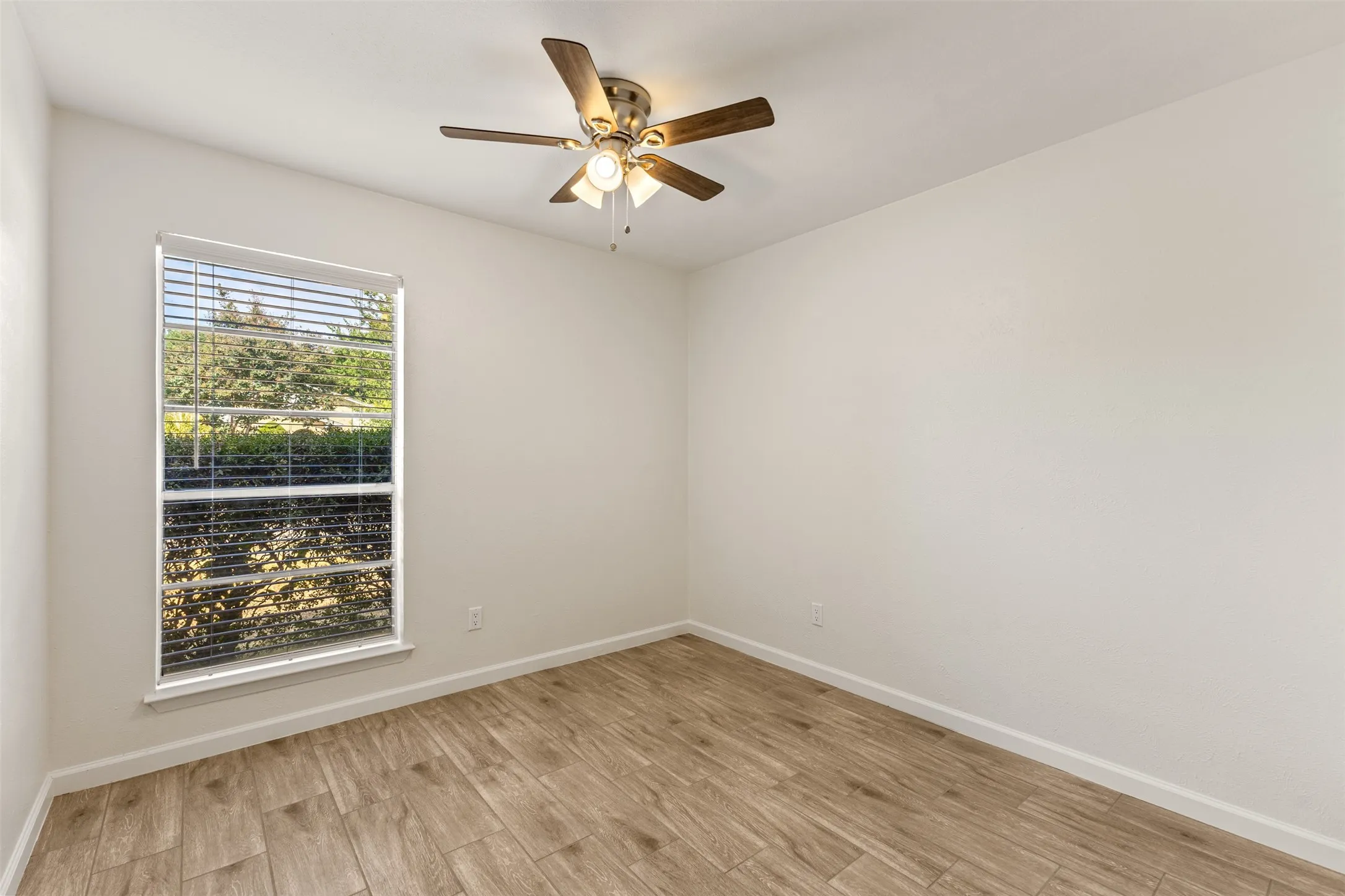 Wood-finish flooring, single window, venetian blinds, ceiling-mounted fan with integrated lighting, neutral wall paint