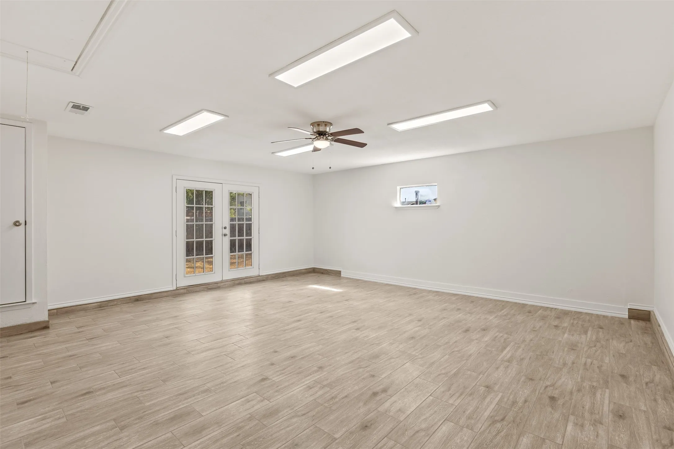 Spacious room featuring wood-look tile flooring, white walls, and a ceiling fan