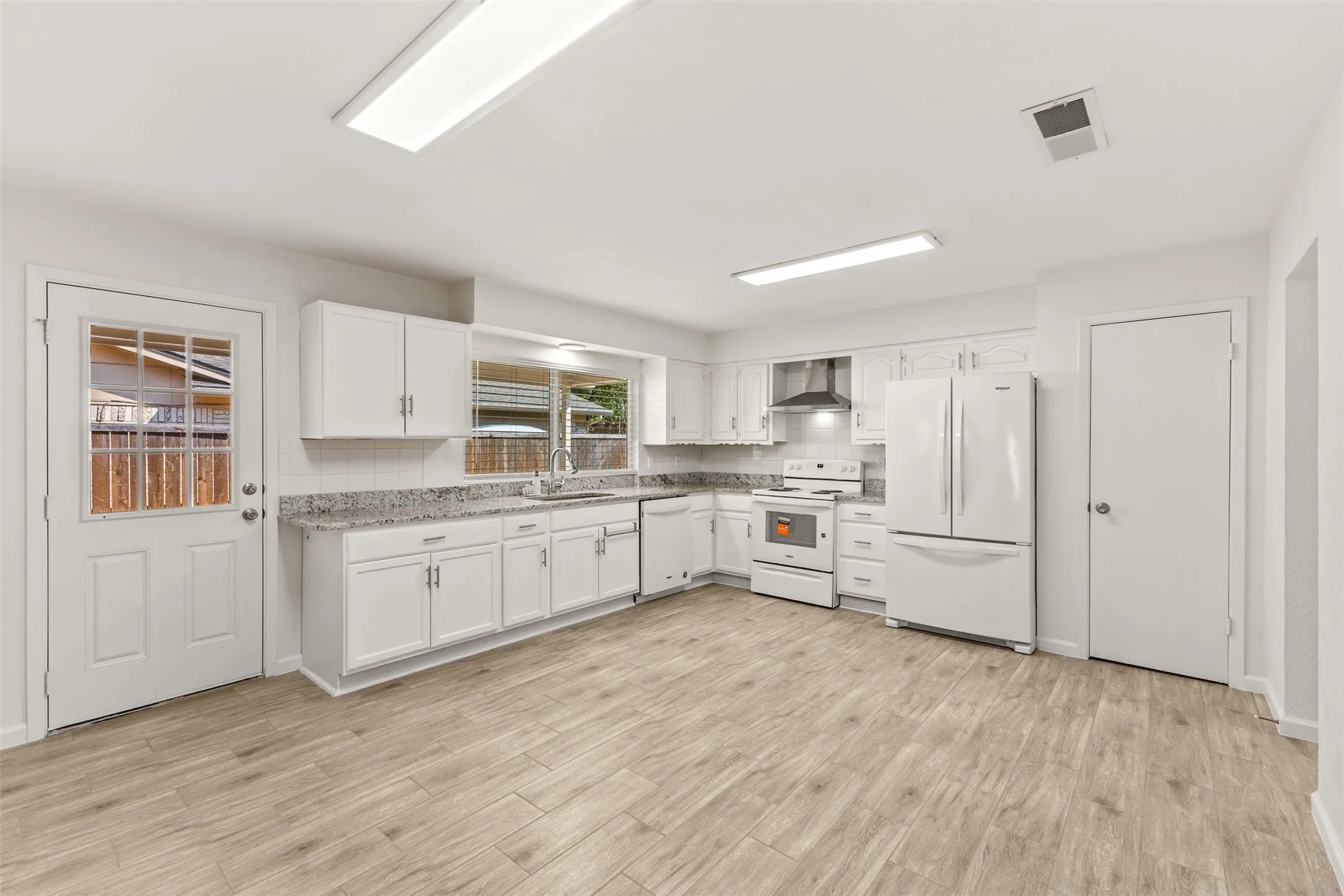 Spacious kitchen featuring white cabinetry, a tile backsplash, light-toned countertops, and wood-finish flooring