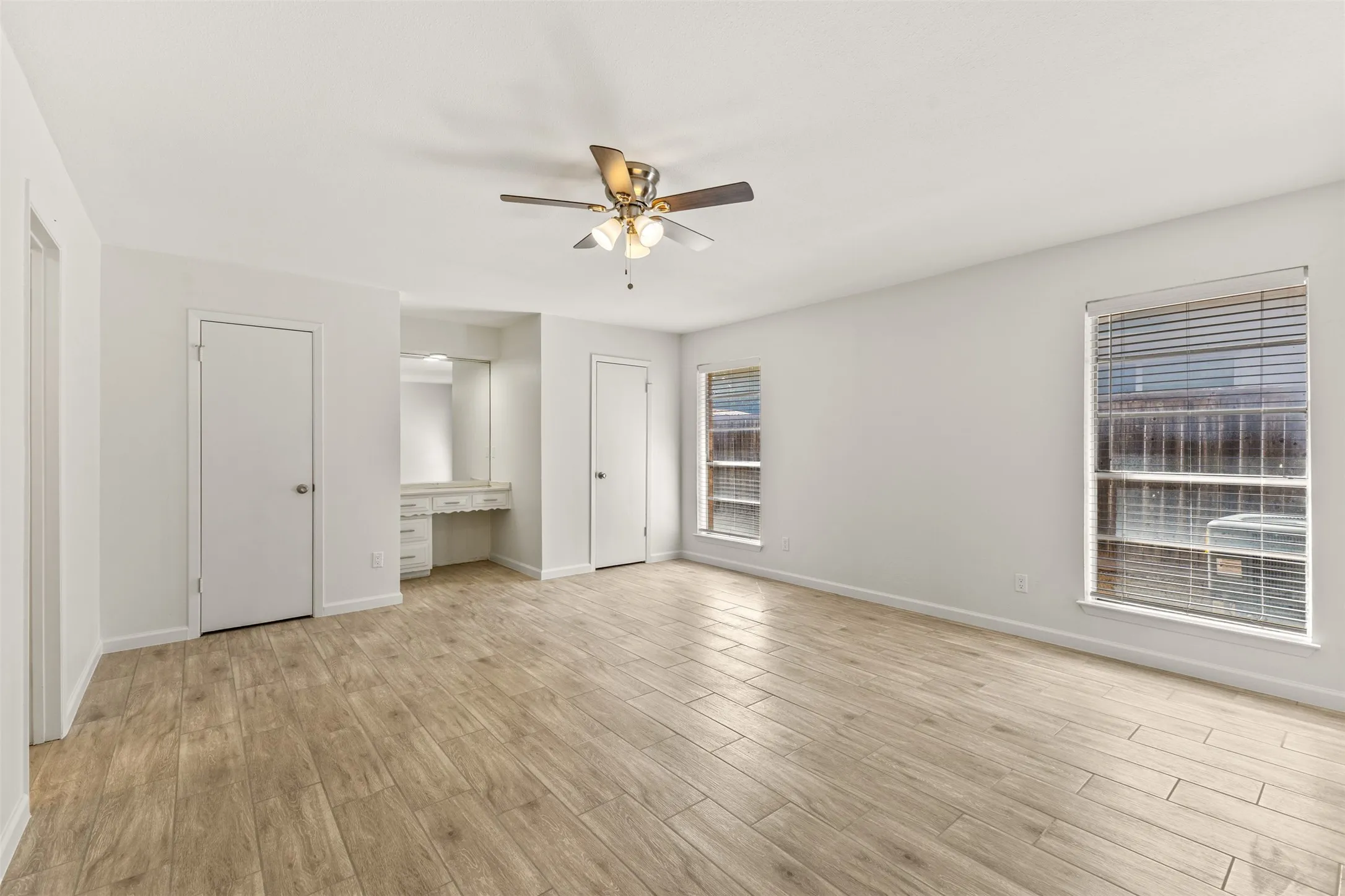 Wood-finish flooring, built-in vanity with mirror, ceiling fan with integrated lighting, and multiple windows