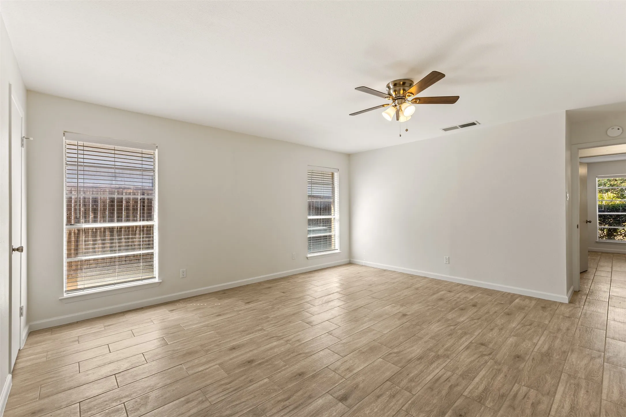 Open-concept room featuring light-toned wood-finish flooring, multiple windows, and a ceiling fan with integrated lighting