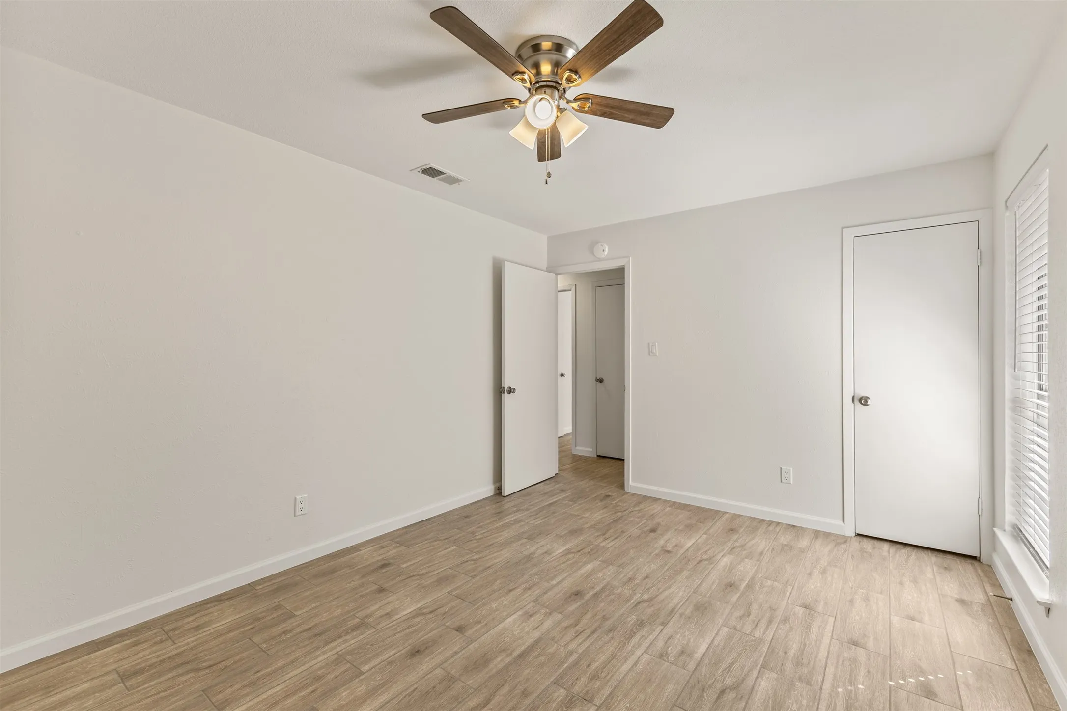 Light-filled room featuring wood-finish flooring, a ceiling fan with integrated lighting, and white paneled doors