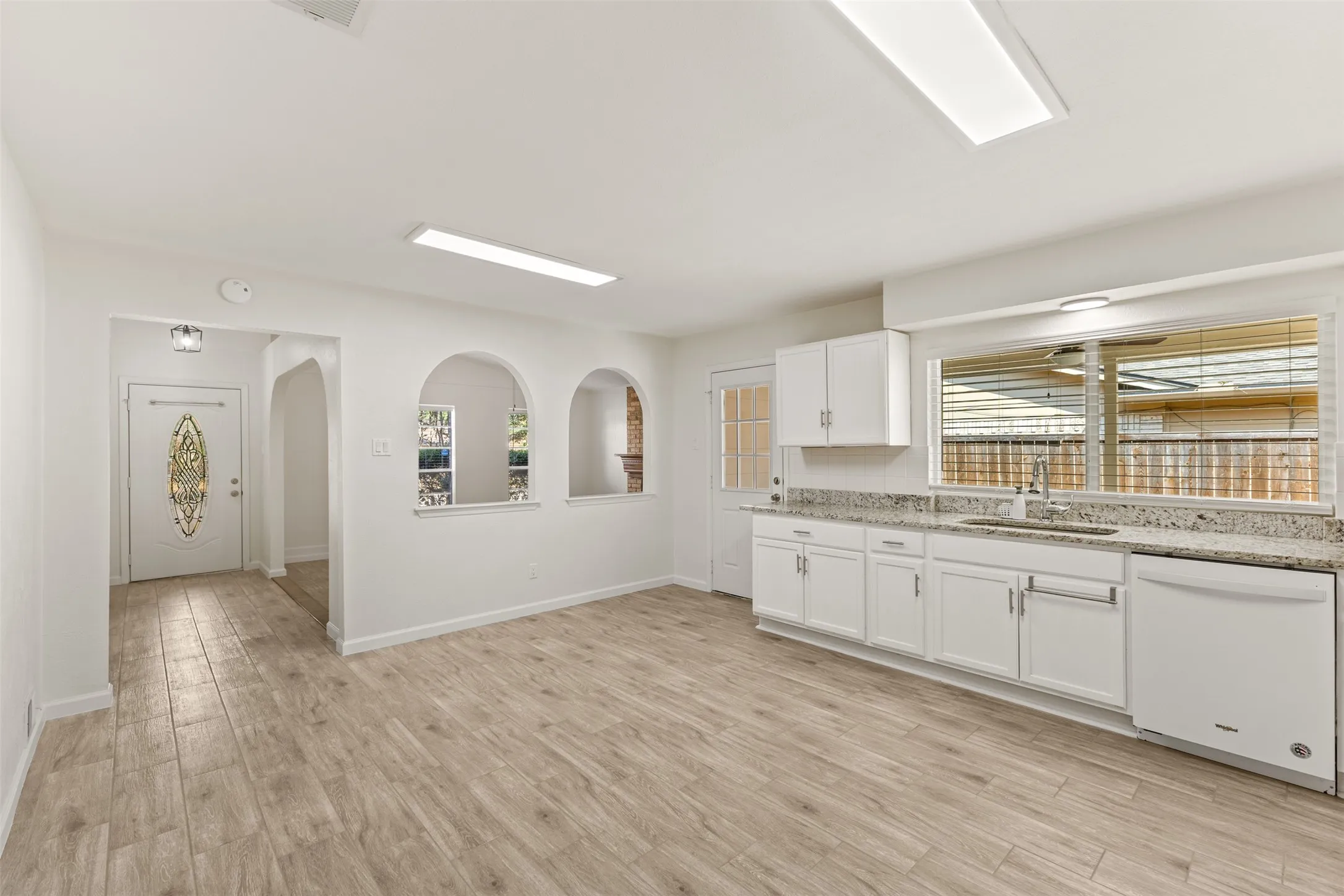 Wood-finish flooring throughout, kitchen with white cabinetry, light-toned countertops, and a full-size dishwasher