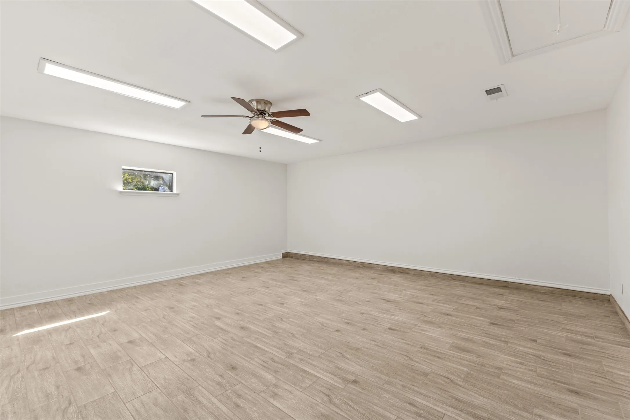 Spacious room featuring wood-finish flooring, multiple recessed light panels, a ceiling fan, and a single window