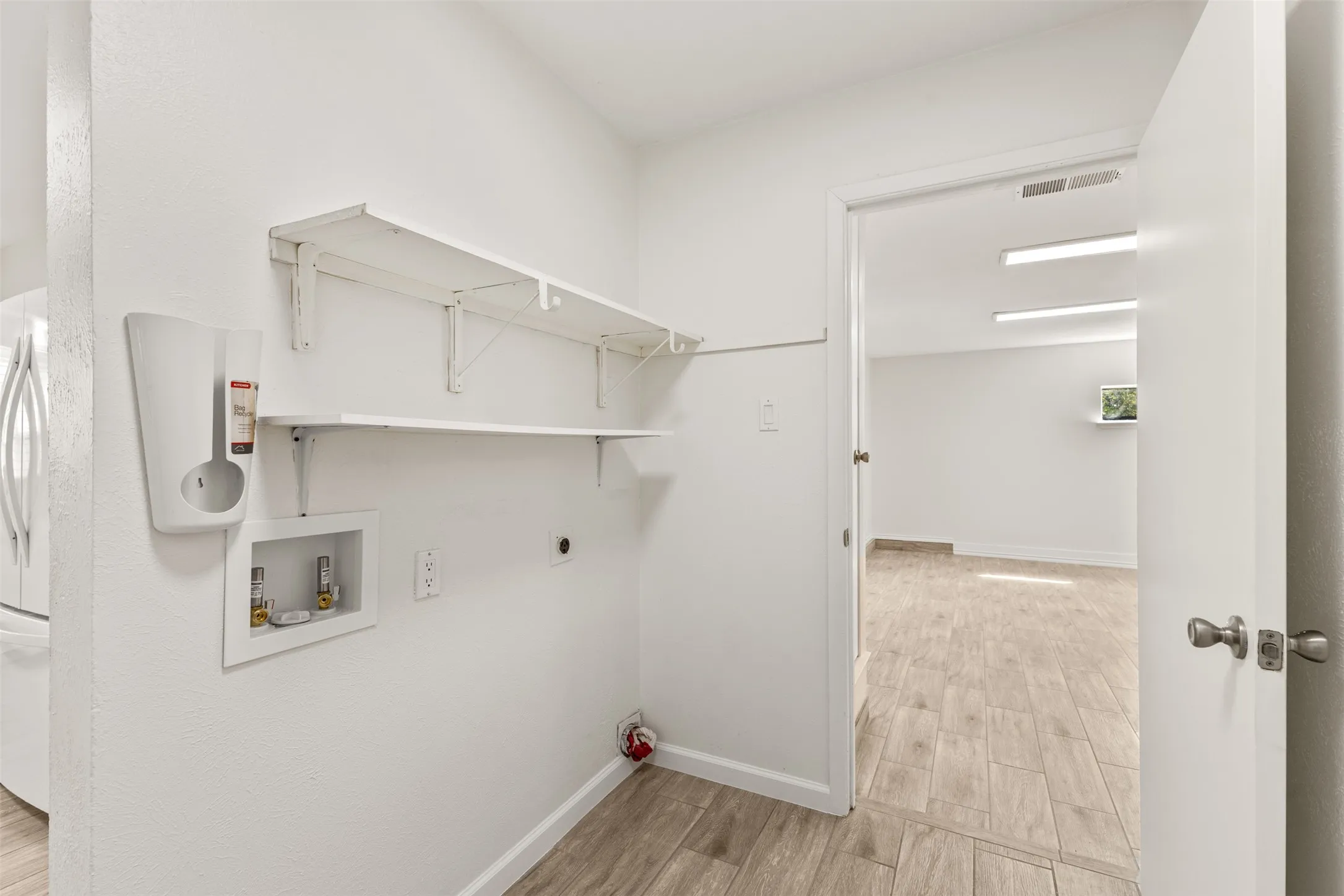 Utility area featuring wood-finish flooring, white walls, and built-in shelving