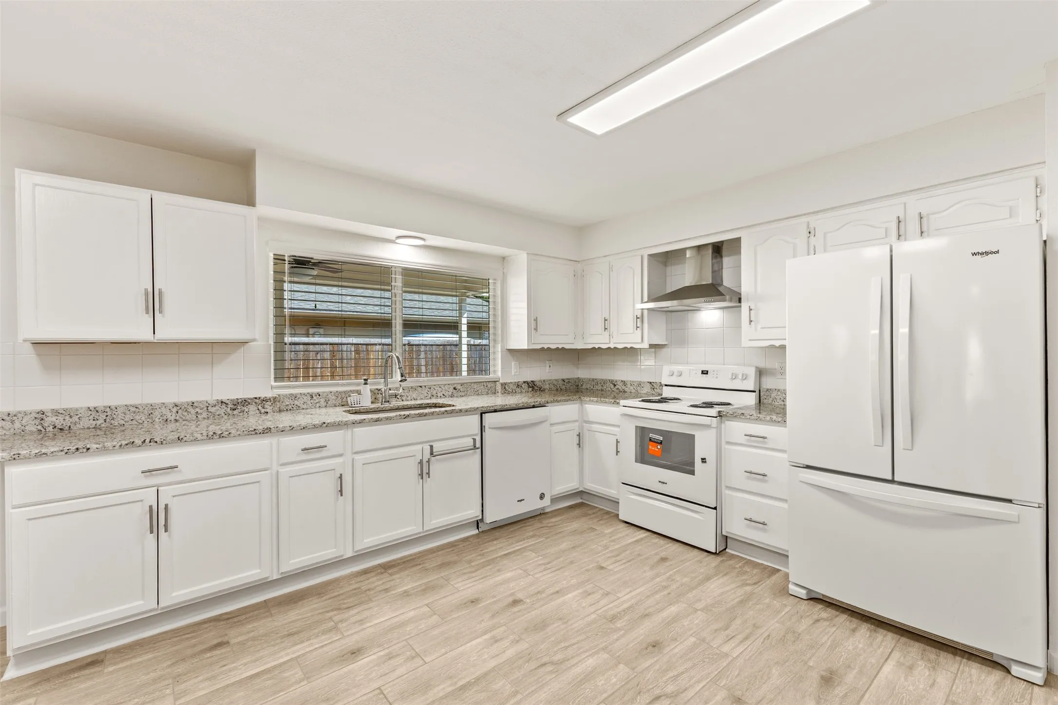 White cabinetry, wood-finish flooring, white appliances, and a window above the sink