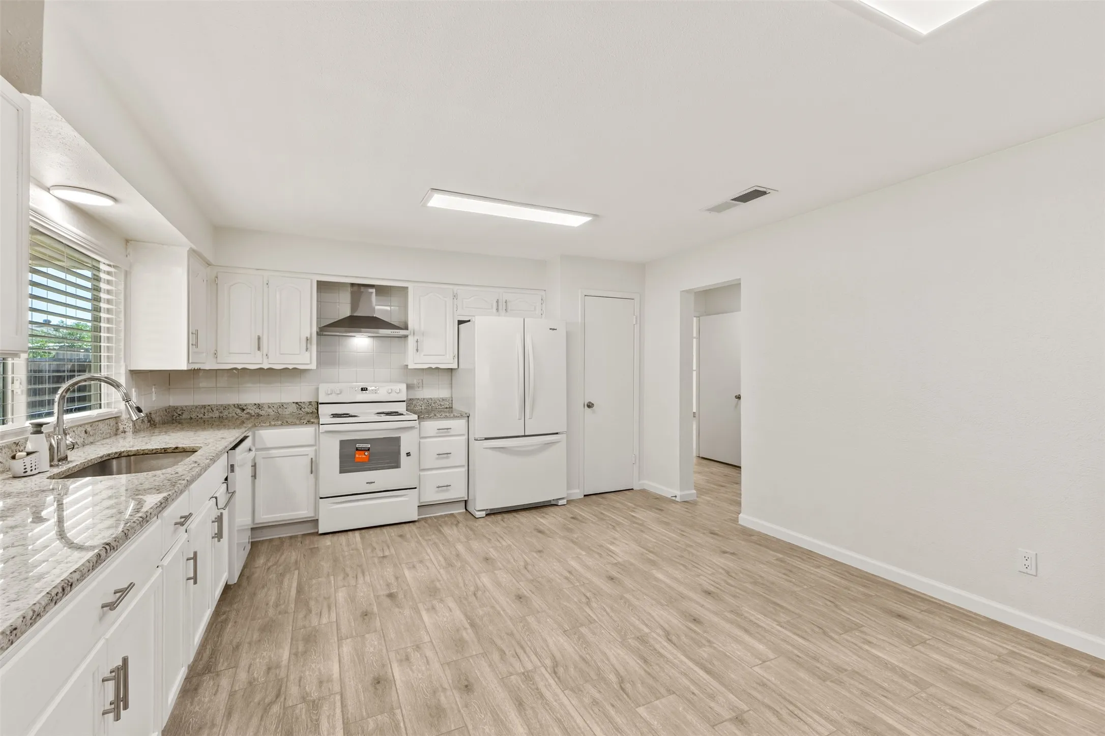Kitchen featuring wood-finish flooring, white cabinetry with modern hardware, granite countertops, and a white appliance suite