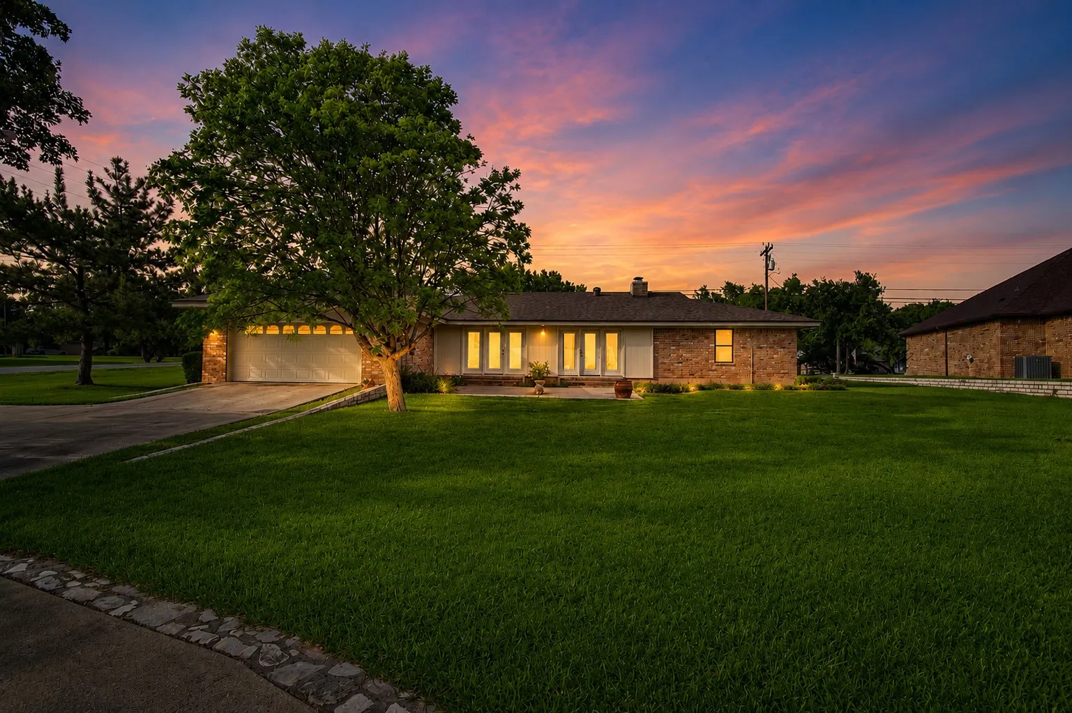 Brick exterior with a large front lawn, attached garage, and mature tree landscaping
