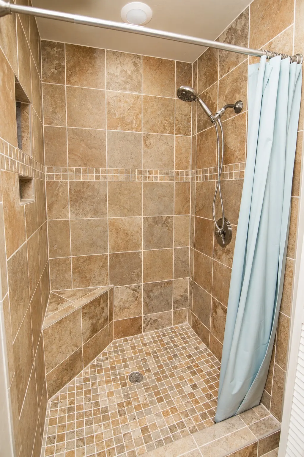 Tiled shower with a built-in bench, recessed shelf, mosaic tile floor, and a handheld showerhead