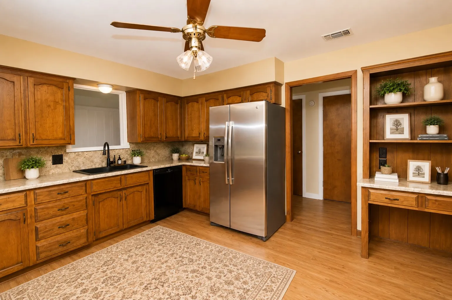 Warm wood cabinetry with stainless steel appliances and tile backsplash, hardwood flooring throughout, ceiling fan with integrated lighting, and built-in shelving with display space