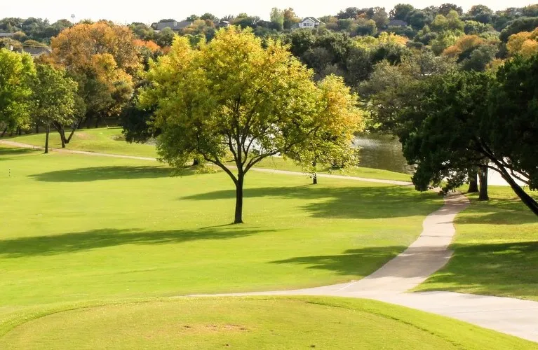 Manicured green spaces with mature trees, paved pathways, and a tranquil pond