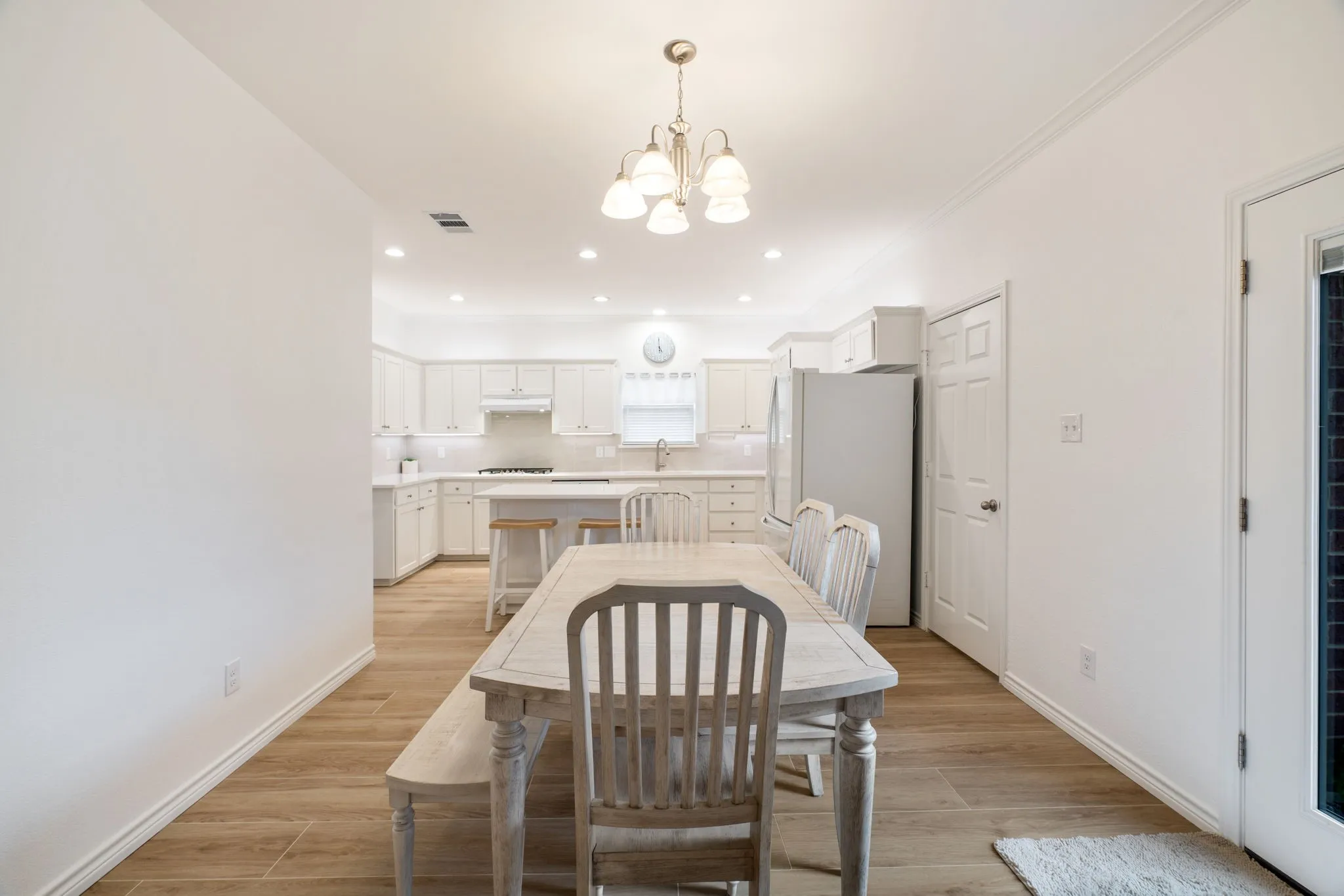 Recessed lighting, wood-finish flooring, white cabinetry, island with seating, and a pendant light fixture