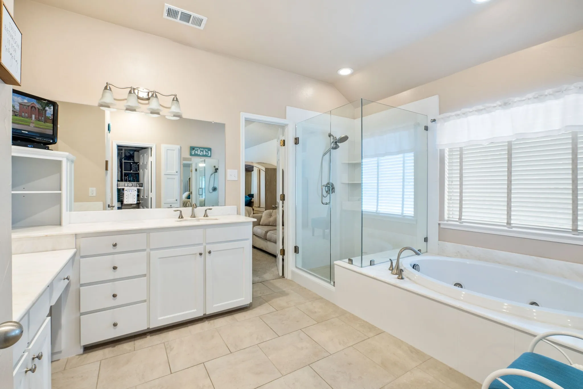 Built-in vanity with white cabinetry and integrated sink, large mirror with vanity lighting, glass-enclosed shower, built-in soaking tub, and tile flooring