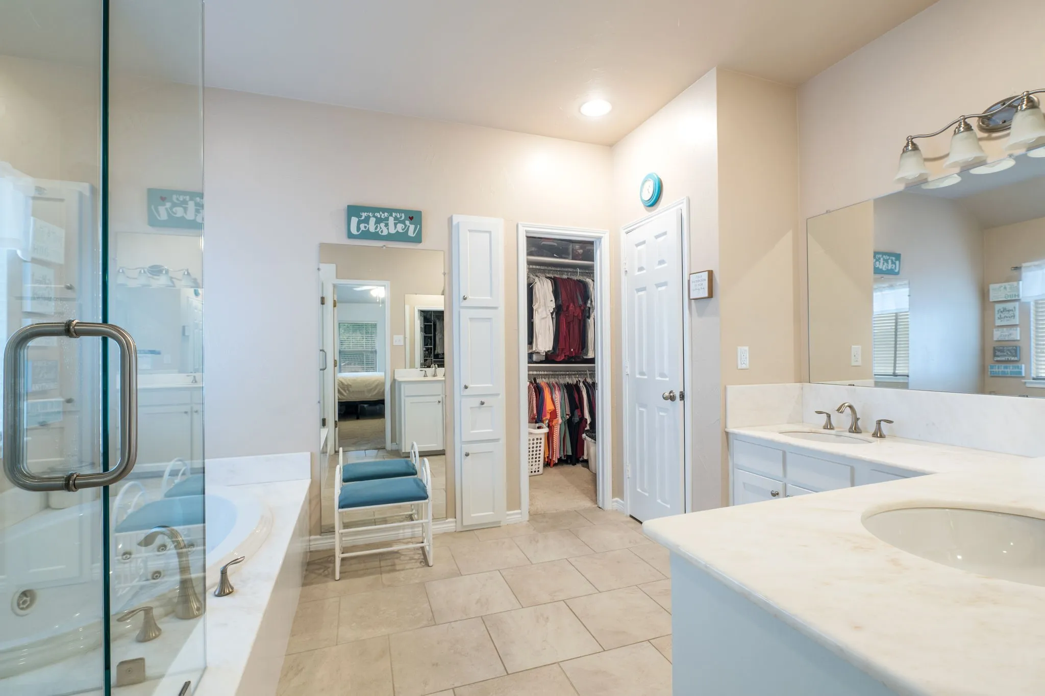 Spacious bathroom featuring a glass-enclosed shower, built-in soaking tub, dual vanity with undermount sinks, and a large walk-in closet
