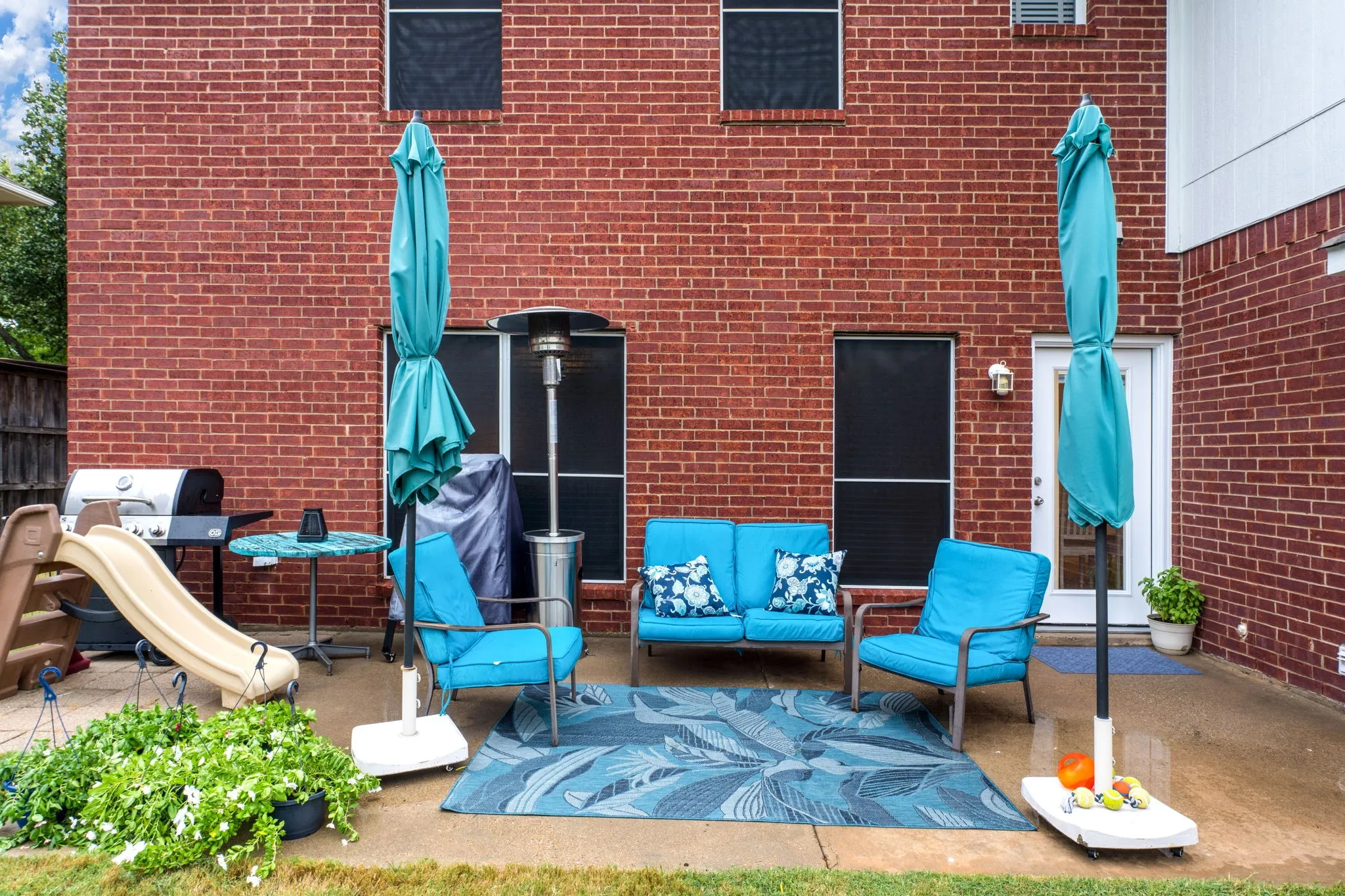 Brick exterior with multiple windows and a white exterior door opening to a concrete patio