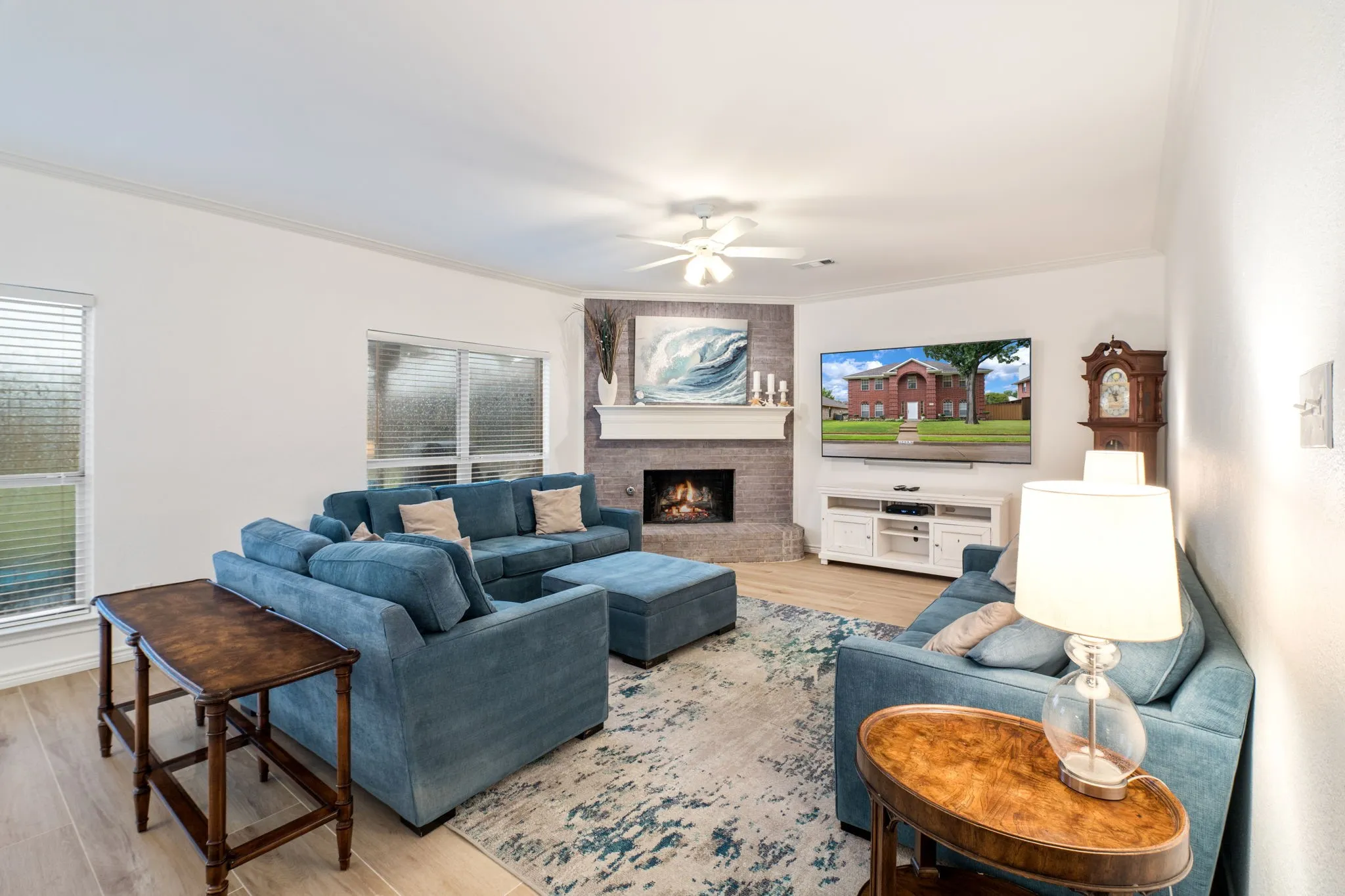 Living area featuring a corner fireplace with a white mantel, textured stone surround, wood-finish flooring, and a ceiling fan