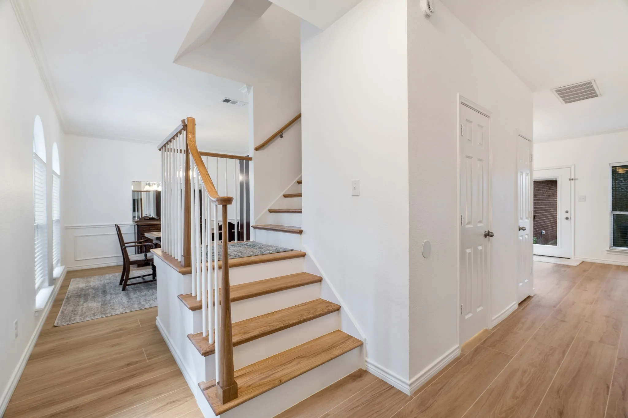 Wood-finish flooring throughout, staircase with wood-finish treads and white risers, white paneled doors, and arched windows