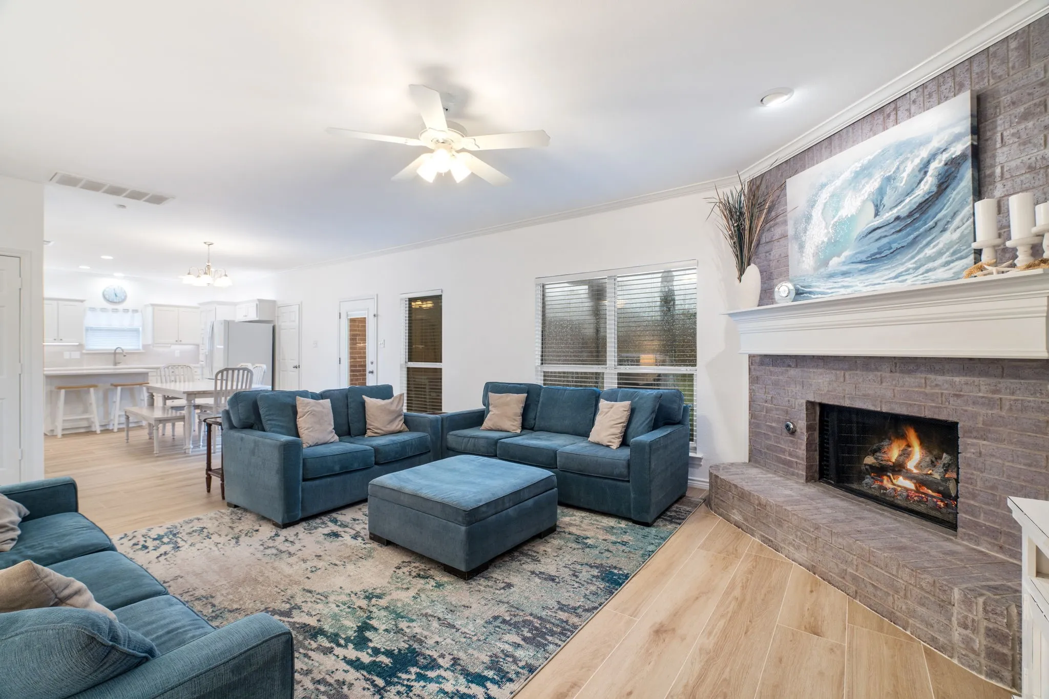Spacious living area featuring light wood-finish flooring and a brick-surround fireplace with a mantel