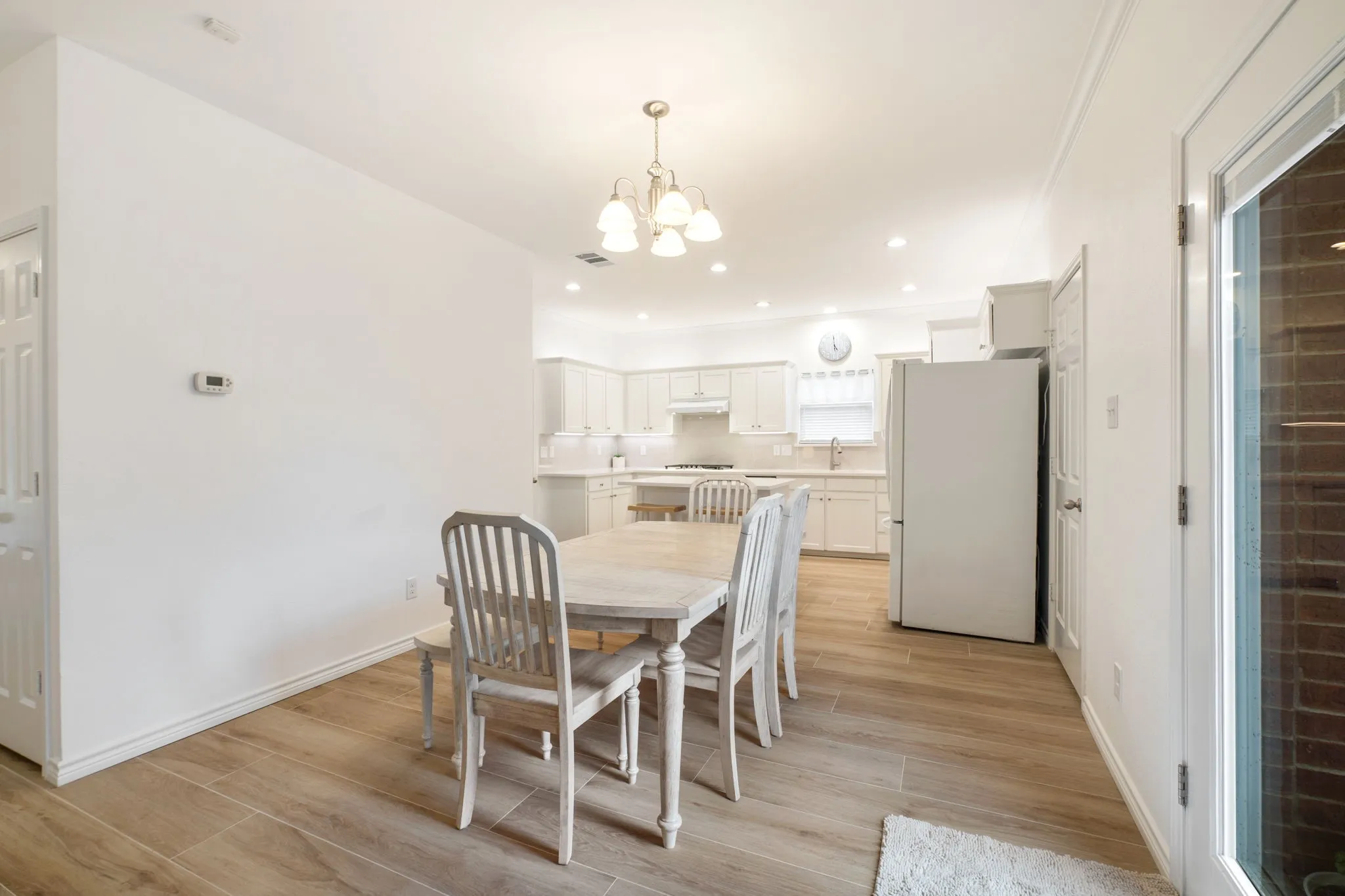 Wood-finish flooring throughout, white interior walls, and a white kitchen with recessed lighting