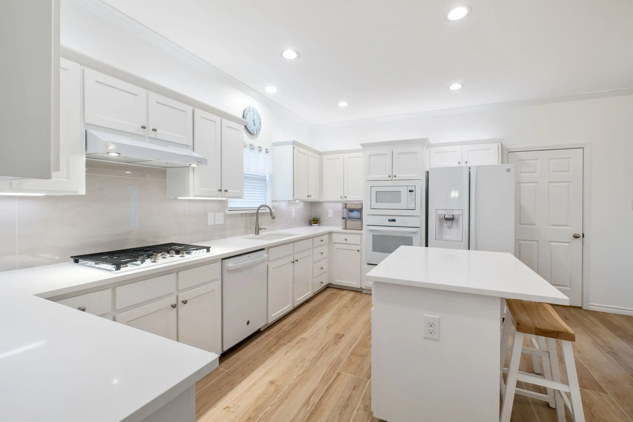 Light wood-finish flooring, white cabinetry, integrated stainless steel appliances, recessed ceiling lighting, and a center island with a white countertop
