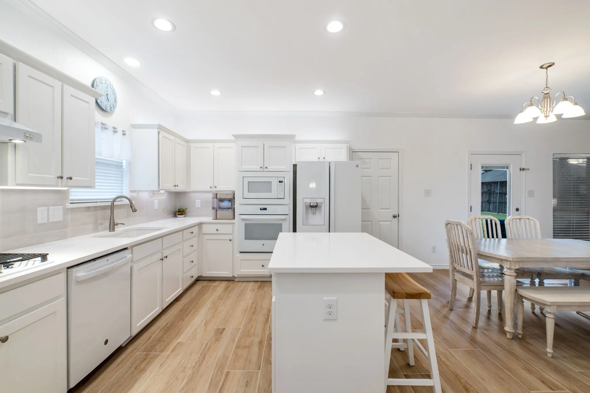 White shaker cabinetry, quartz countertops, tile backsplash, wood-finish flooring, and recessed lighting