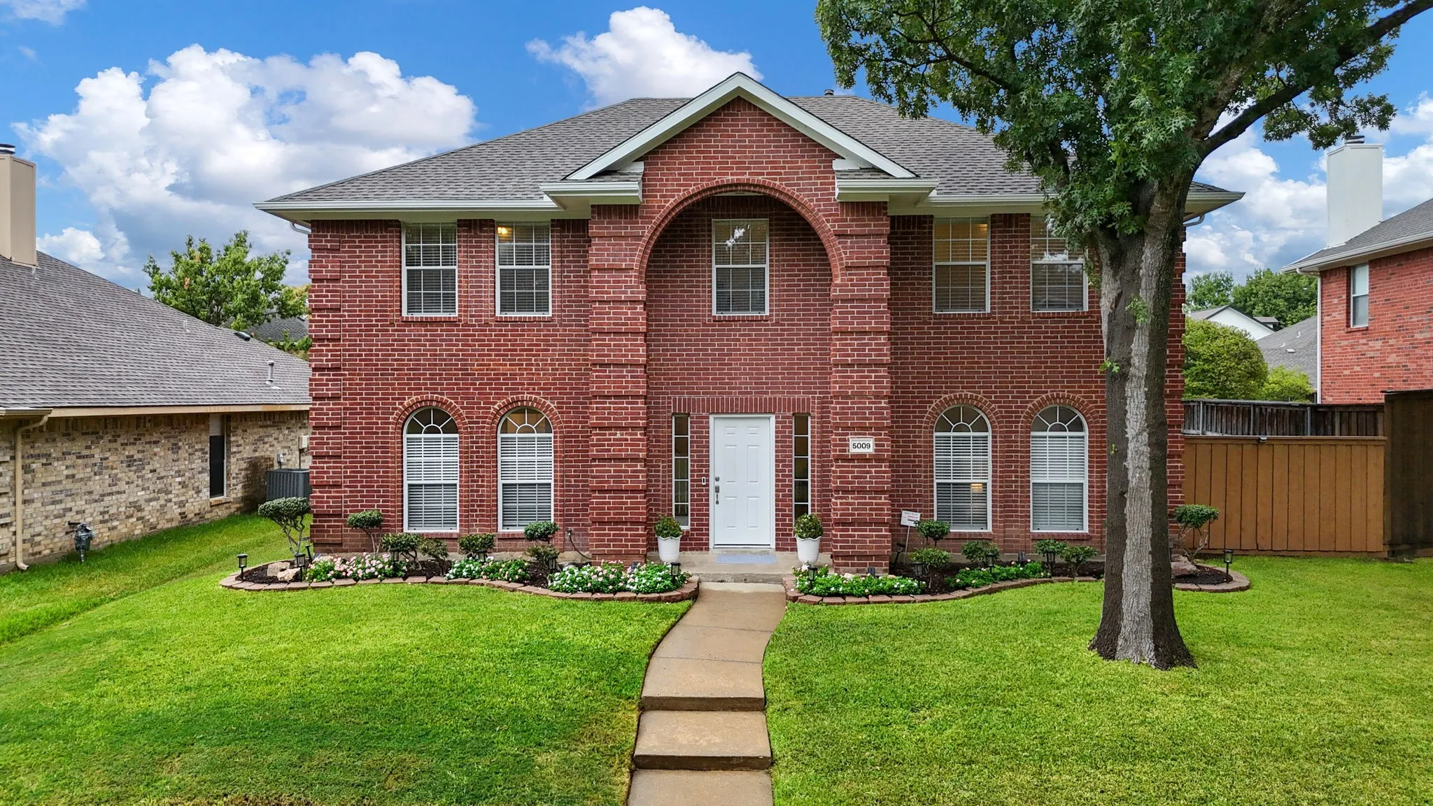 Two-story brick exterior with an arched entryway, multiple arched windows, and a paved walkway