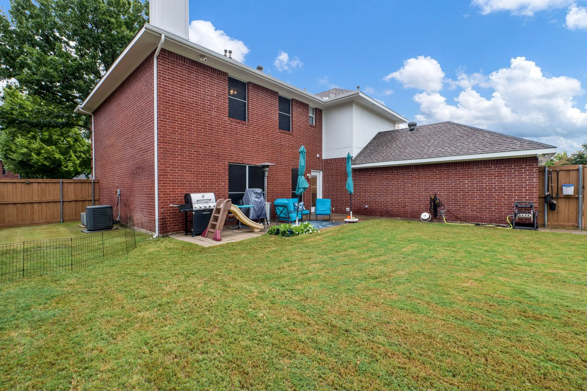 Expansive backyard featuring a manicured lawn, brick exterior, and a concrete patio
