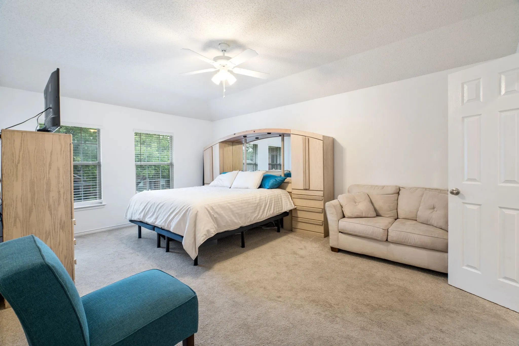 White paneled door opening into a carpeted room with multiple windows, a ceiling fan, and white walls