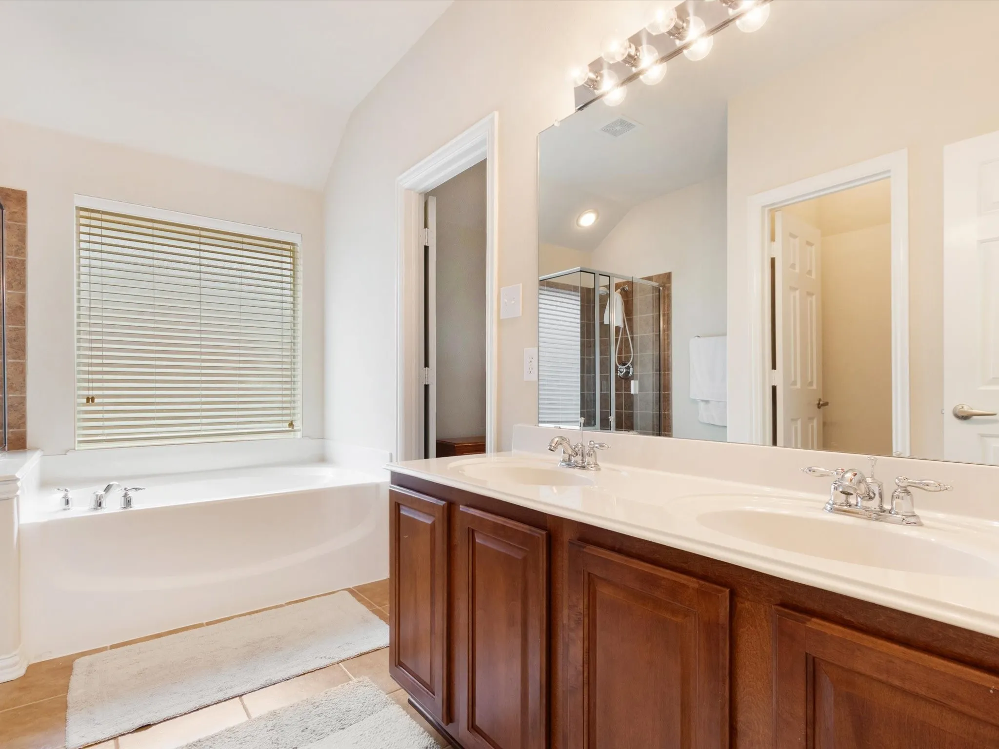 Dual vanity with integrated sinks, a large wall-mounted mirror, and a built-in shower with a glass enclosure