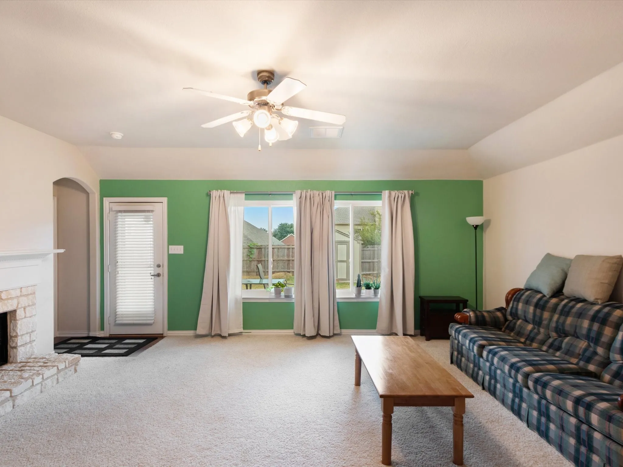 Carpeted living area featuring a fireplace with brick surround, ceiling fan, and multiple windows