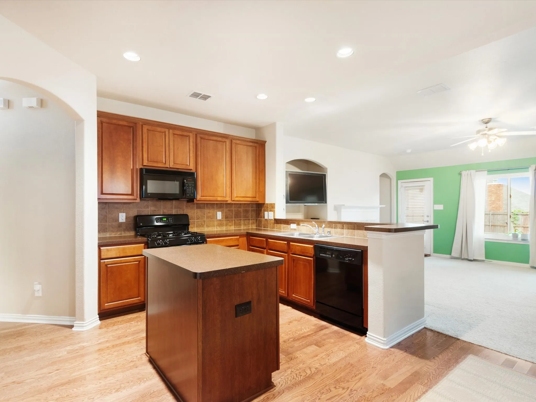 Kitchen featuring wood-finish flooring, a kitchen island, recessed lighting, and black appliances