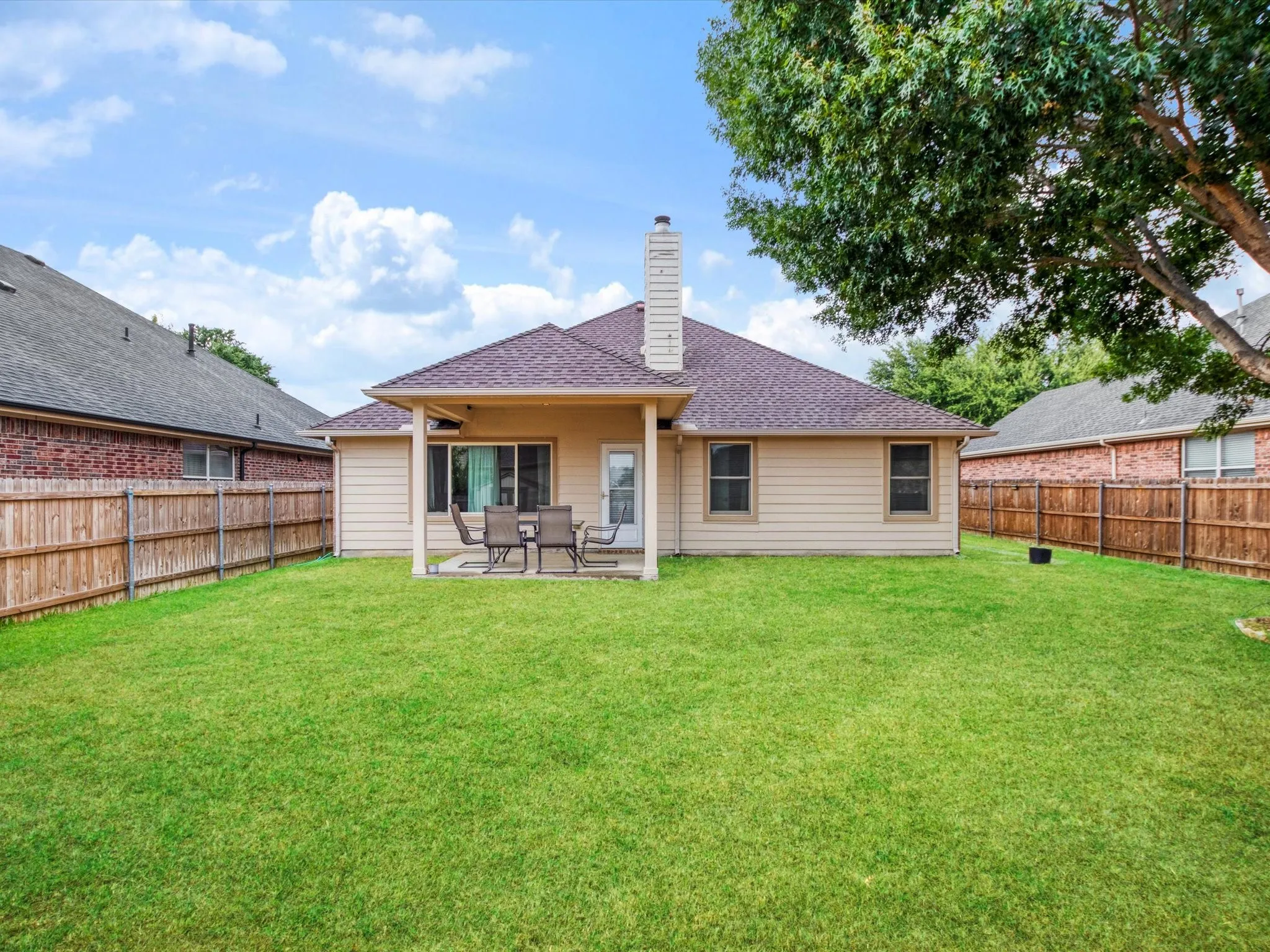 Expansive lawn with a covered patio, featuring a built-in outdoor ceiling fan, and a wood privacy fence