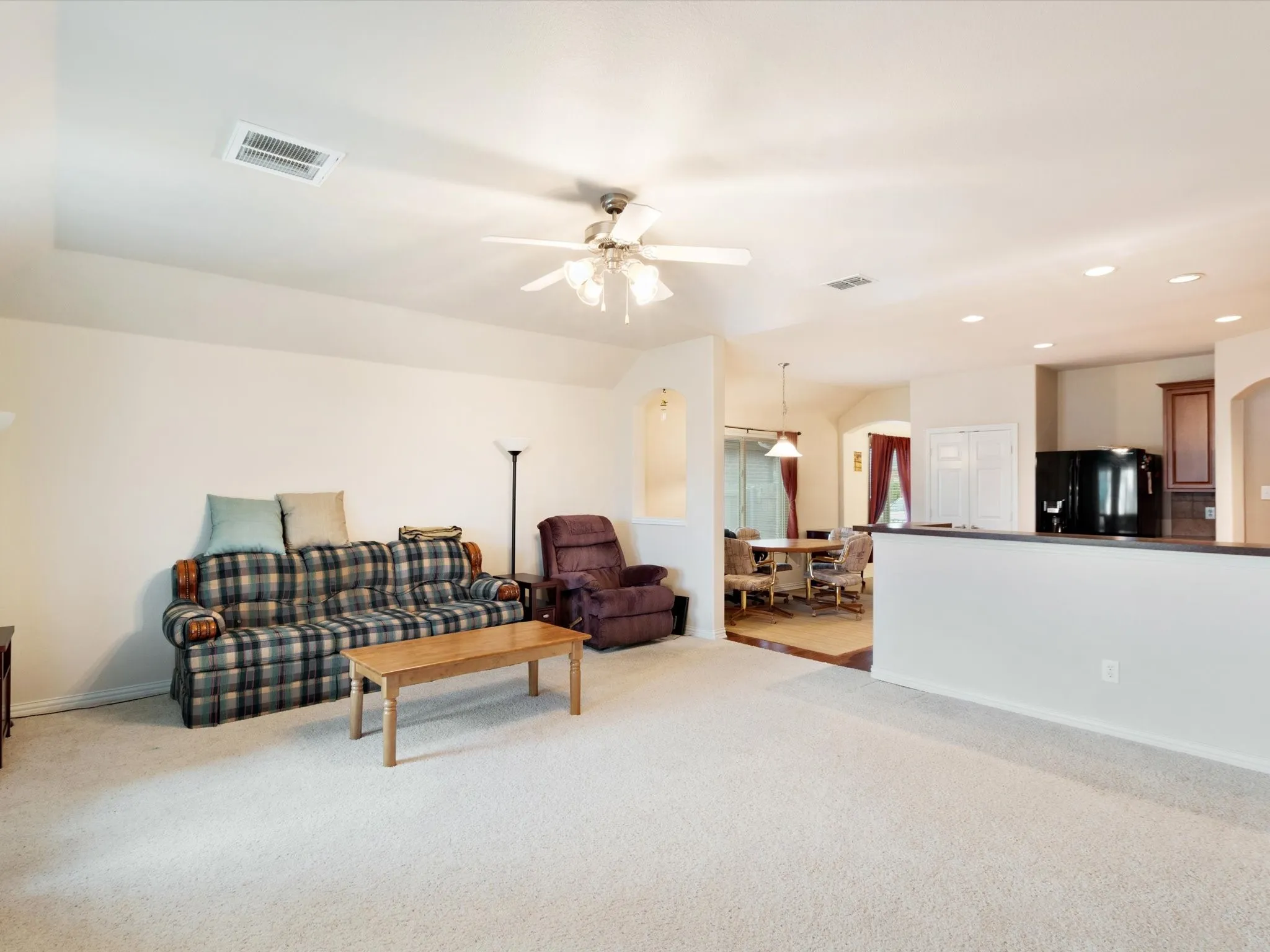 Recessed lighting, ceiling fan, arched doorways, white walls, and a partial wall with a dark countertop