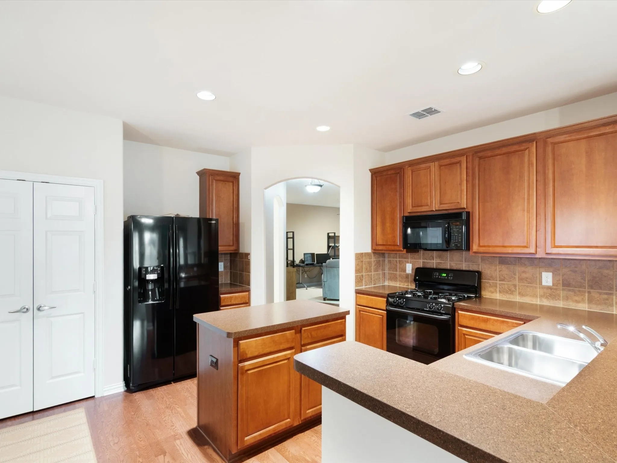 Kitchen featuring wood-finish cabinetry, black appliances, a central island, and a dual basin sink