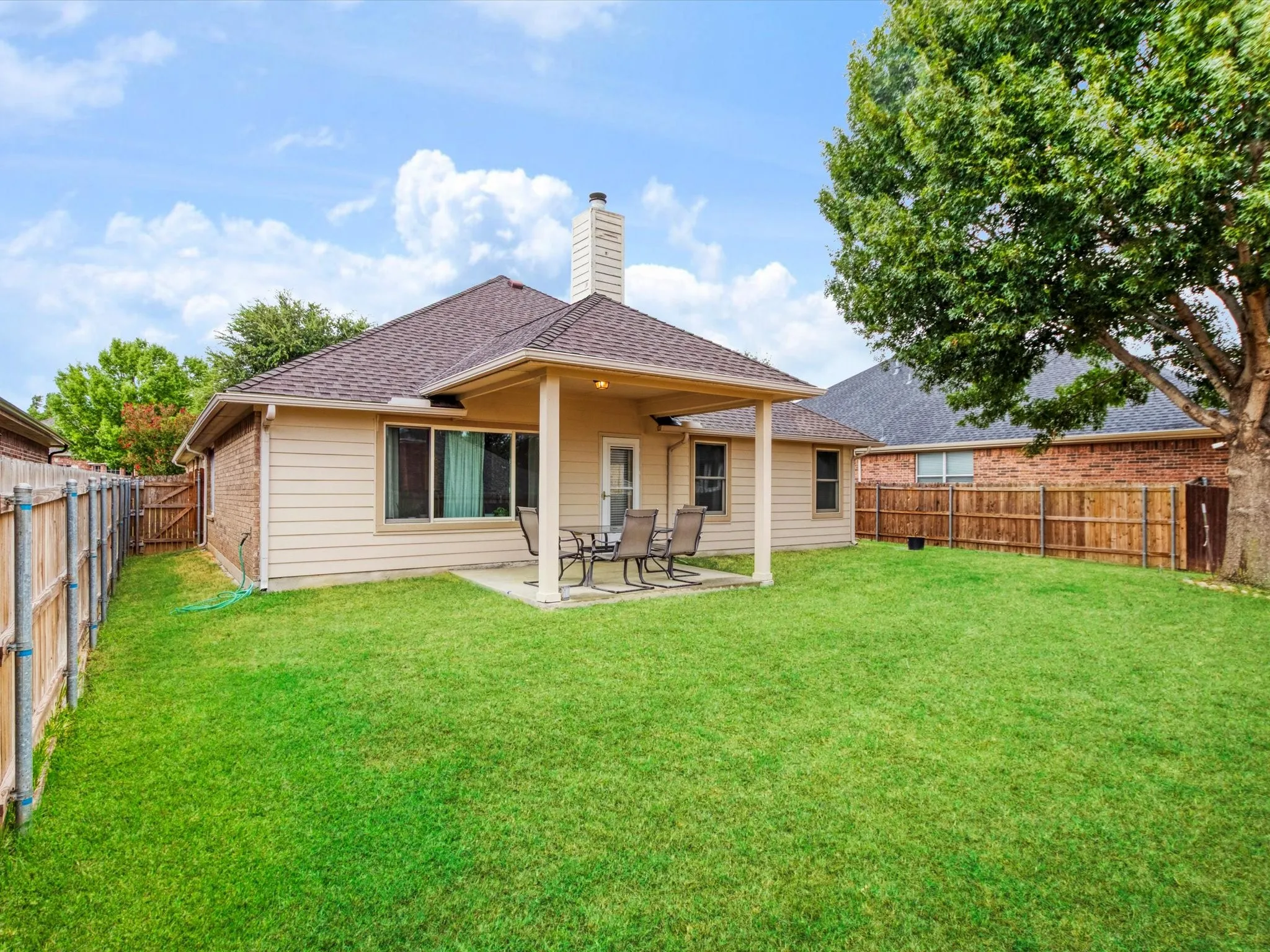 Expansive backyard featuring a covered patio, a mature tree, and privacy fencing
