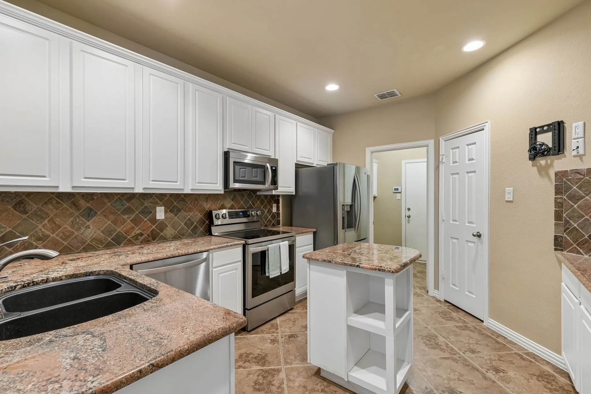 Kitchen featuring white cabinetry, stainless steel appliances, a tile backsplash, granite-style countertops, and a central island with open shelving