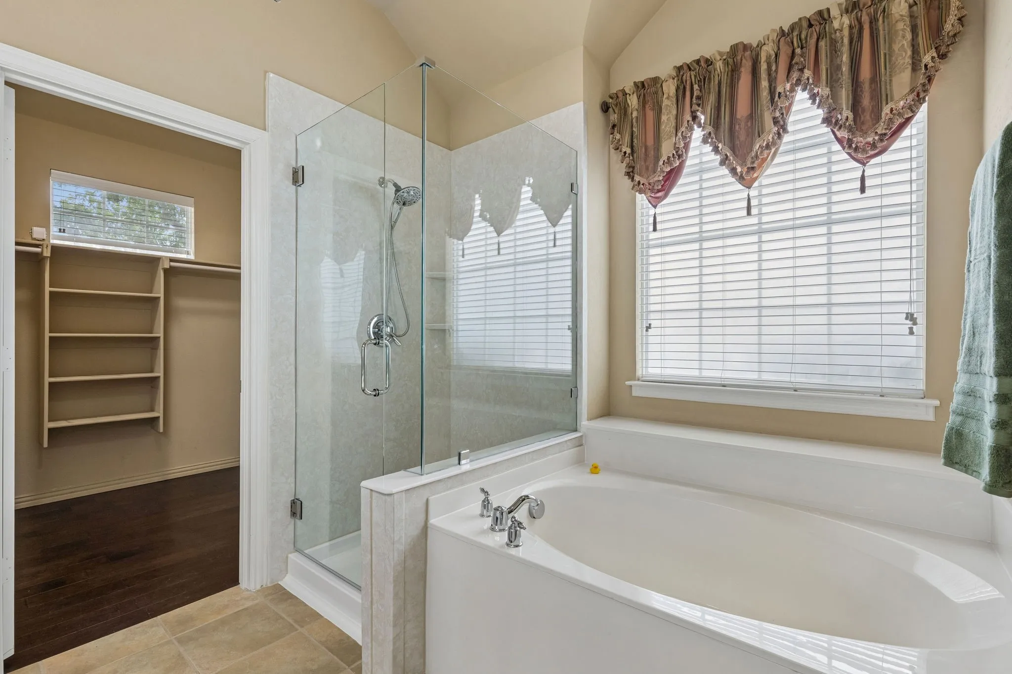 Built-in soaking tub, glass-enclosed shower, and walk-in closet with shelving and wood-finish flooring