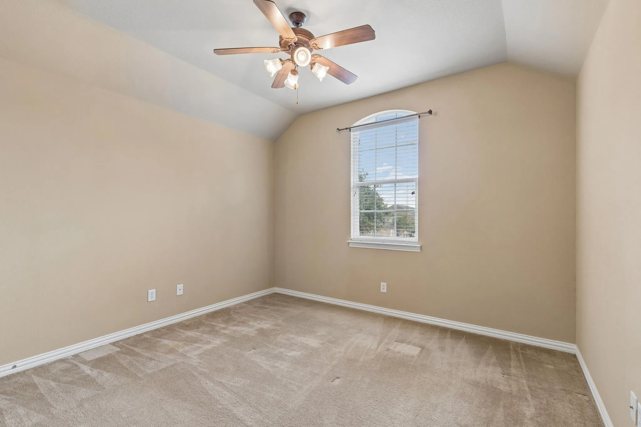 Vaulted ceiling with a ceiling fan, arched window with blinds, and neutral carpeting